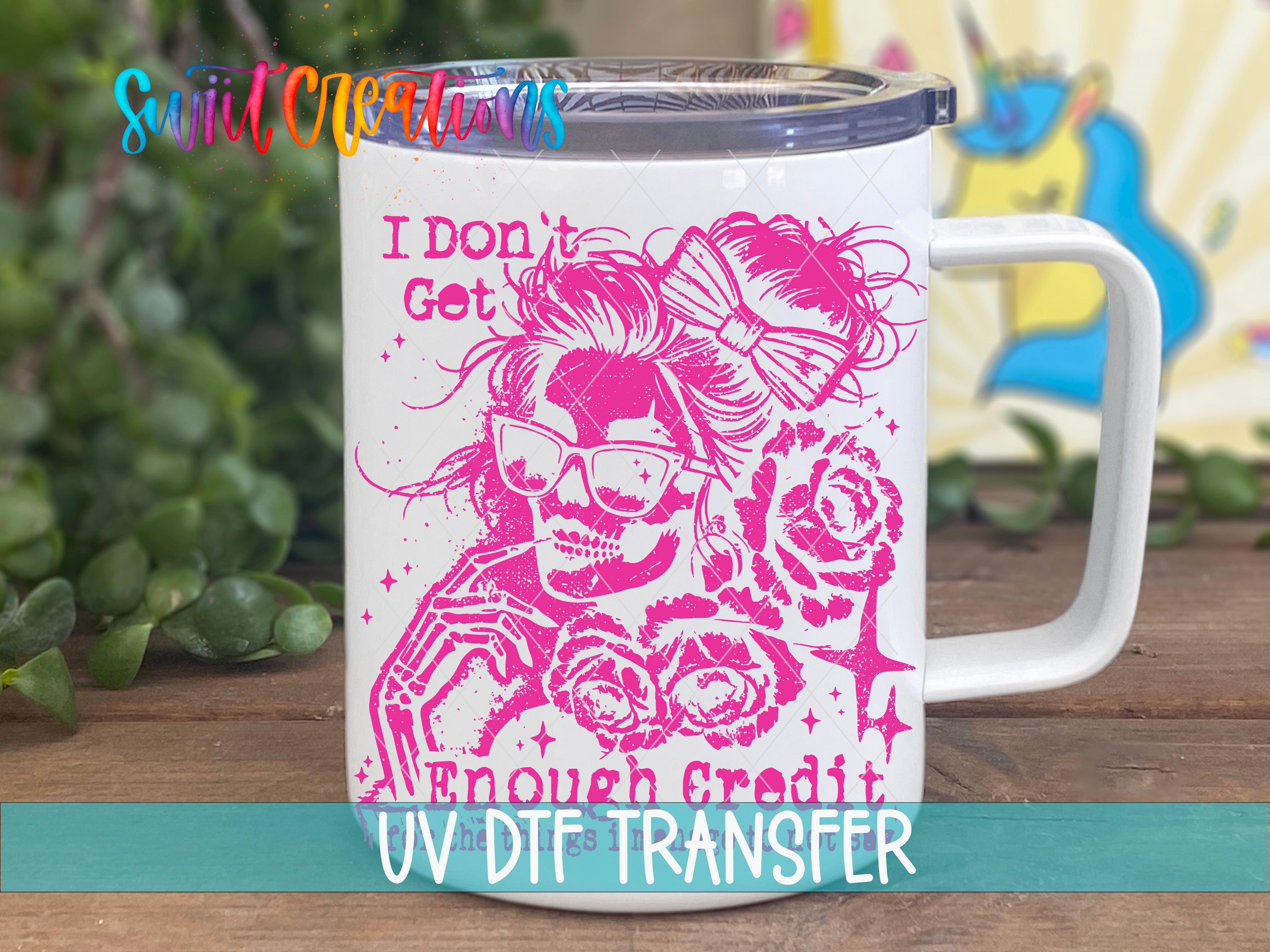 A white mug with a pink design featuring a skull wearing sunglasses and holding flowers, along with the text "I Don't Get Enough Credit" and "UV DTF Transfer".