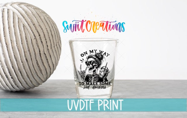 a shot glass with a skull design and text, placed next to a white ball on a gray surface.
