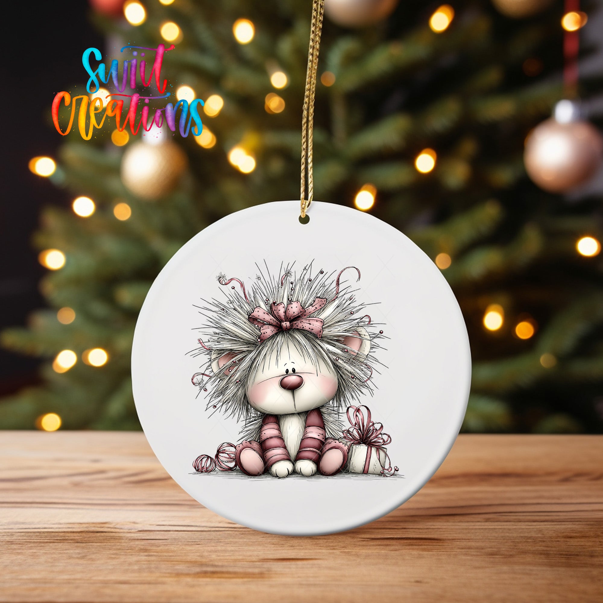 A white ceramic ornament featuring a cartoon illustration of a lion with a bow on its head, sitting on a wooden surface in front of a blurred Christmas tree with twinkling lights.