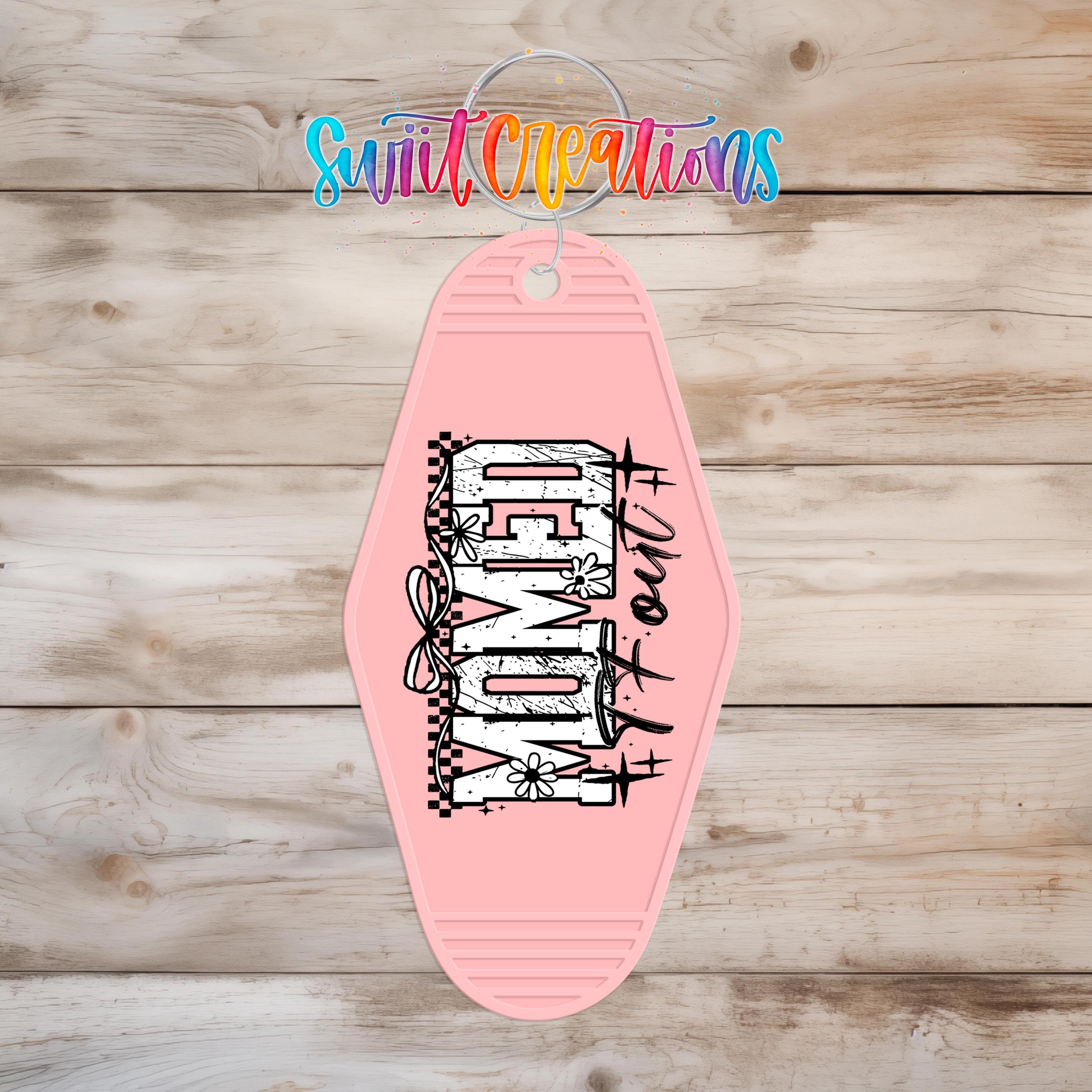 A pink keychain with the word "DOG" printed on it, hanging on a wooden surface.
