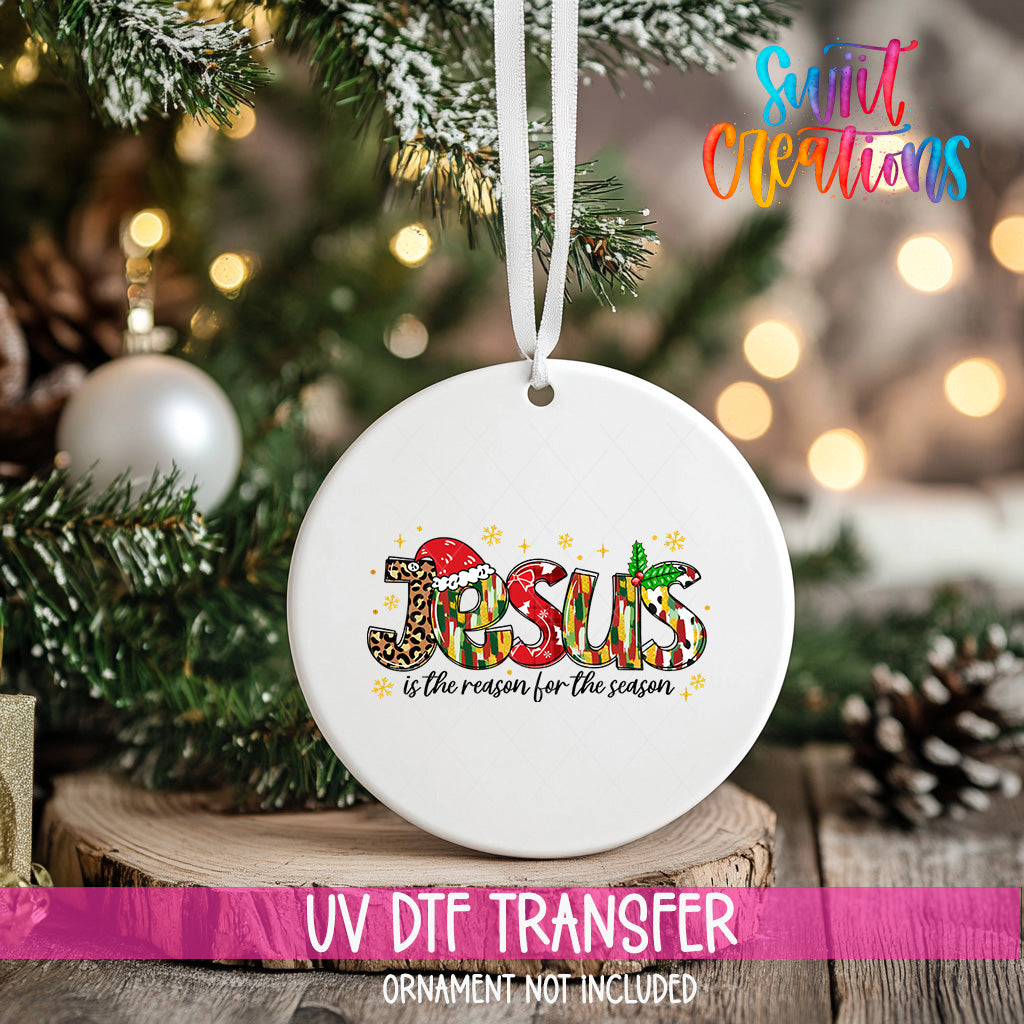 A white ceramic ornament with the word "JESUS" written on it, hanging on a Christmas tree.
