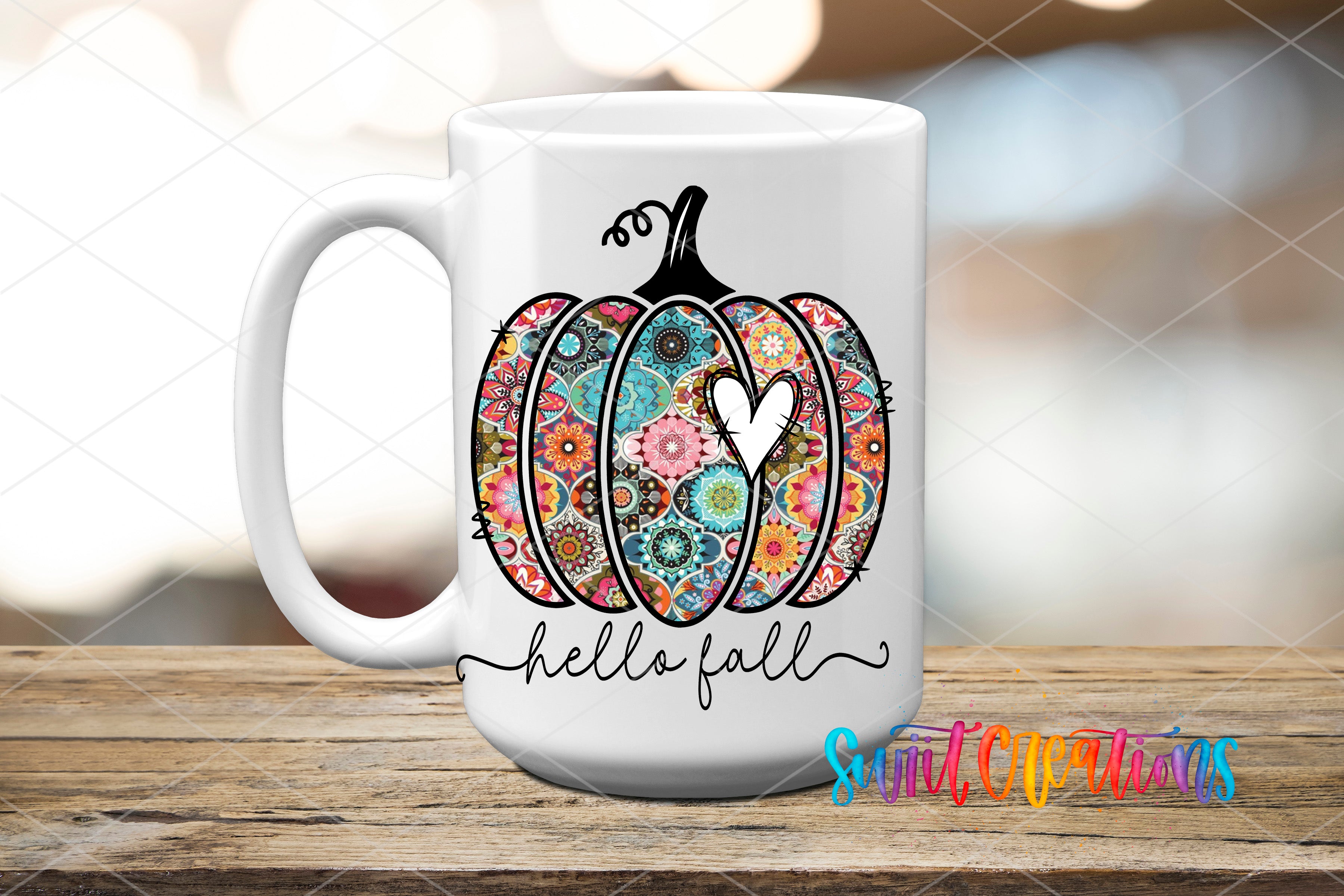 A white ceramic mug with a colorful pumpkin design and the text "Hello fall" printed on it, placed on a wooden surface.