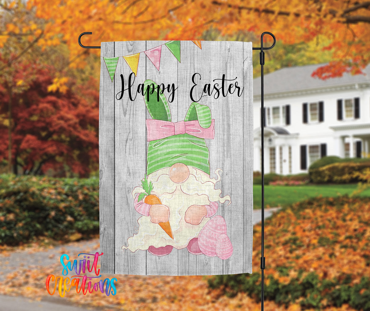 A wooden Easter banner with a gnome holding a carrot and a pink bow, set against a backdrop of colorful autumn foliage and a white house.