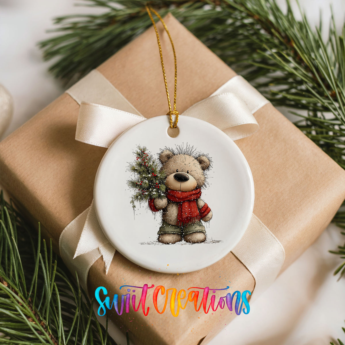 teddy bear in a red scarf holding a Christmas tree ceramic Christmas ornament displayed on a wrapped Christmas gift