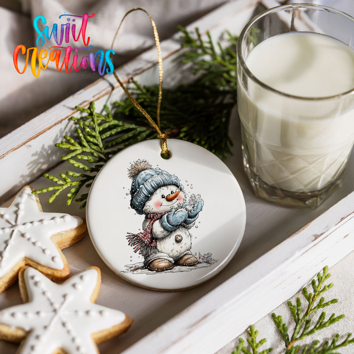 snowman in a blue hat holding a snowball ceramic Christmas ornament styled with holiday cookies and a candle