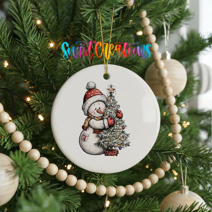 snowman decorating a snowy Christmas tree ceramic Christmas ornament hanging on a green Christmas tree