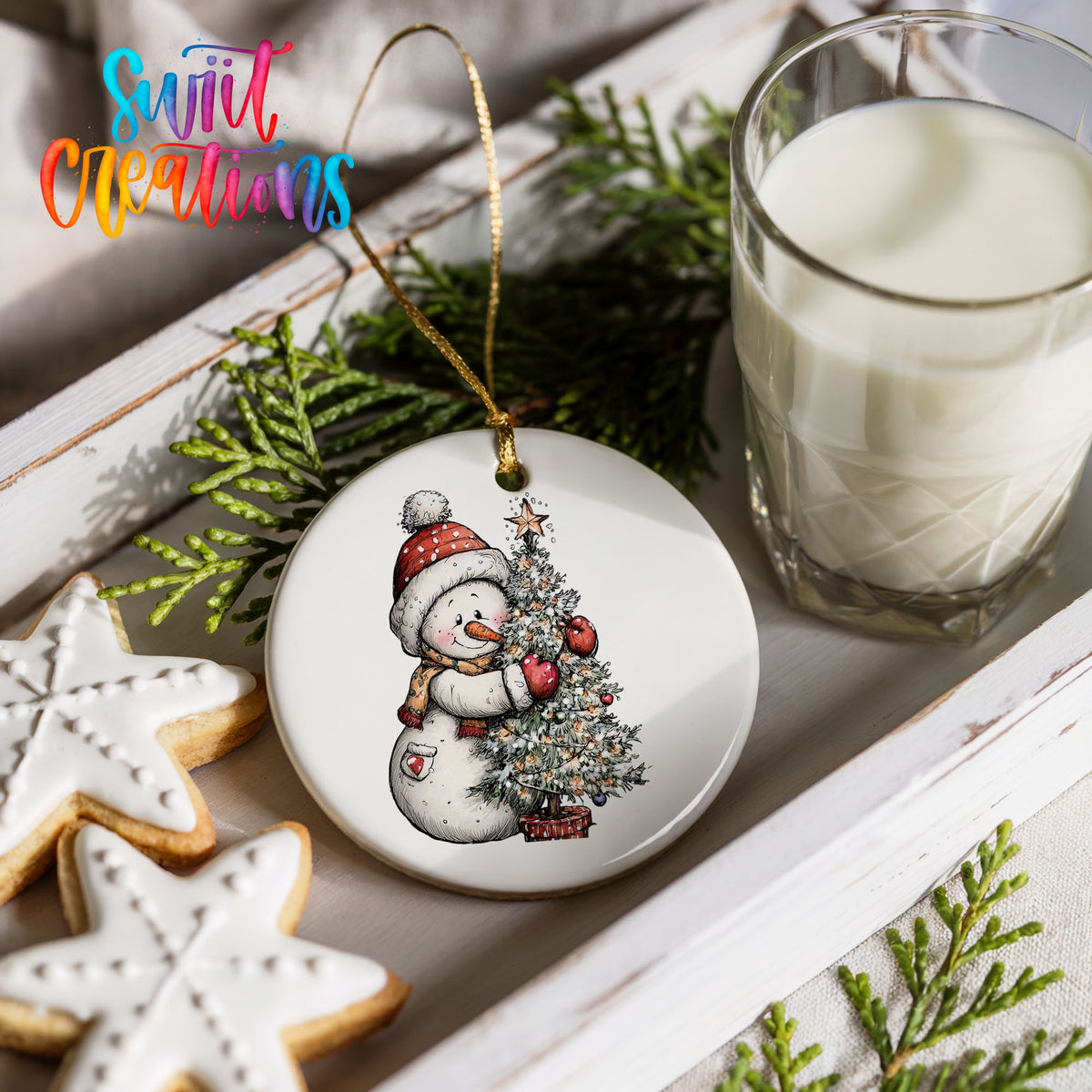 snowman decorating a snowy Christmas tree ceramic Christmas ornament styled with holiday cookies and a candle
