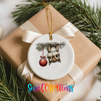 woodland owl hanging upside down with a red ornament ceramic Christmas ornament displayed on a wrapped Christmas gift