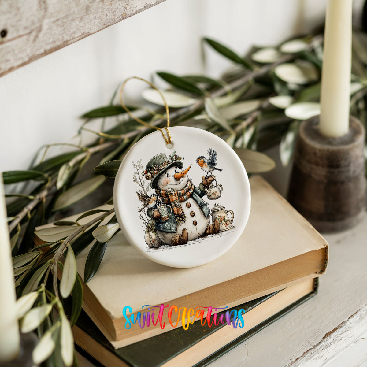 snowman with a lantern and winter birds ceramic Christmas ornament styled on stacked books with greenery