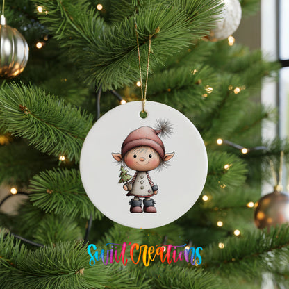 A white ceramic ornament featuring a cartoon elf holding a Christmas tree is hanging on a decorated Christmas tree.