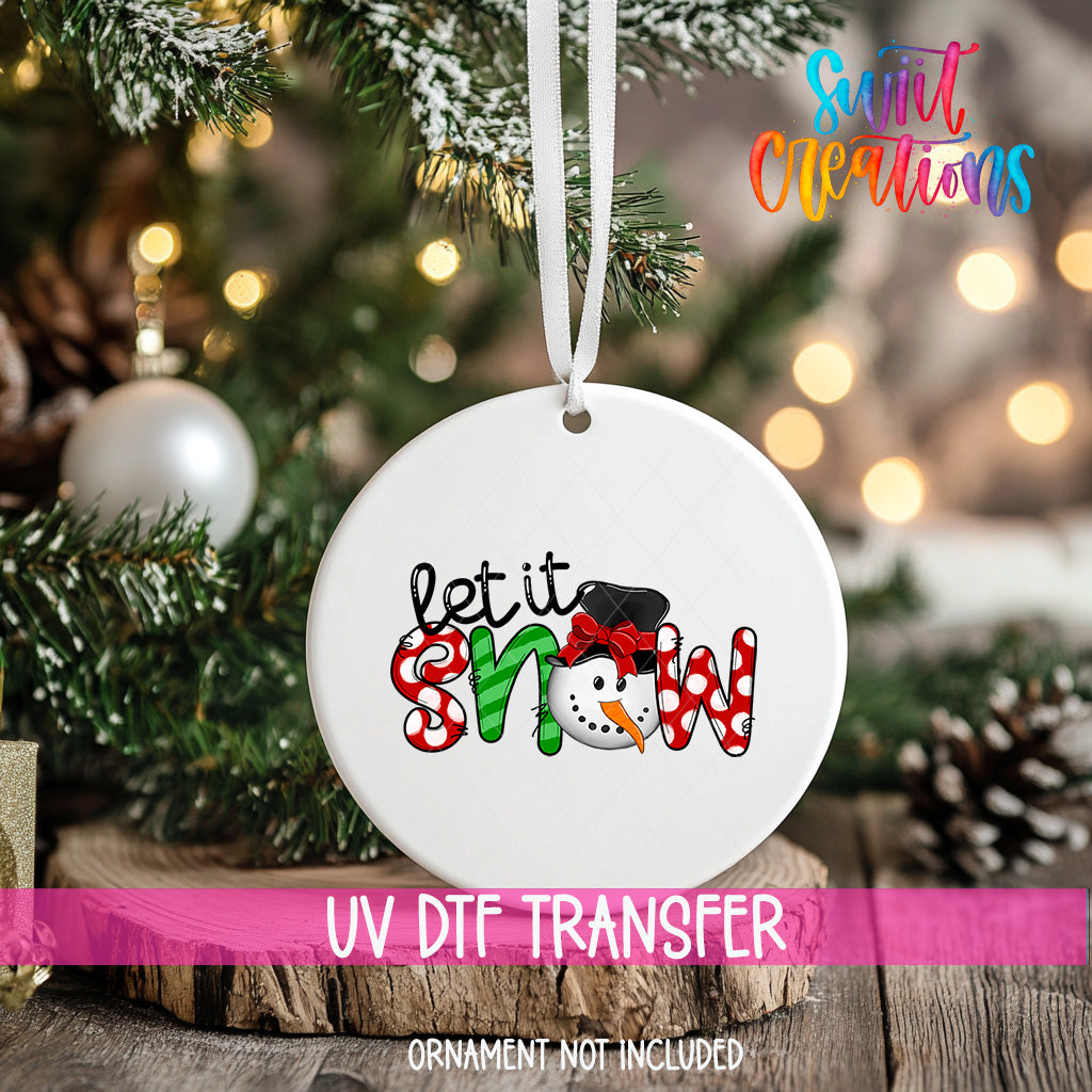 A white ornament with the text "let it snow" and a snowman graphic hangs on a Christmas tree.