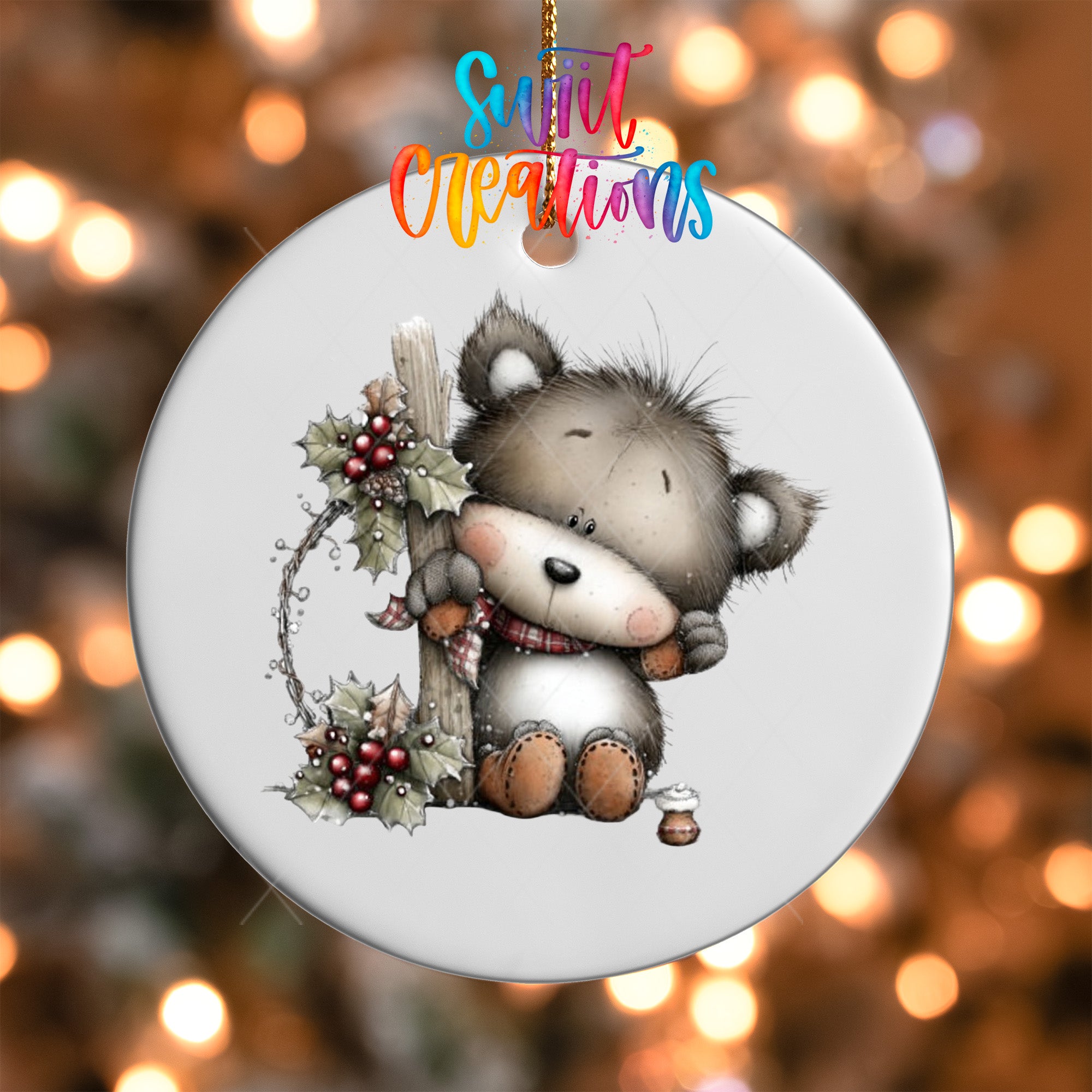 A white ornament with a cute bear holding a holly leaf and berries, surrounded by a festive background of twinkling lights.