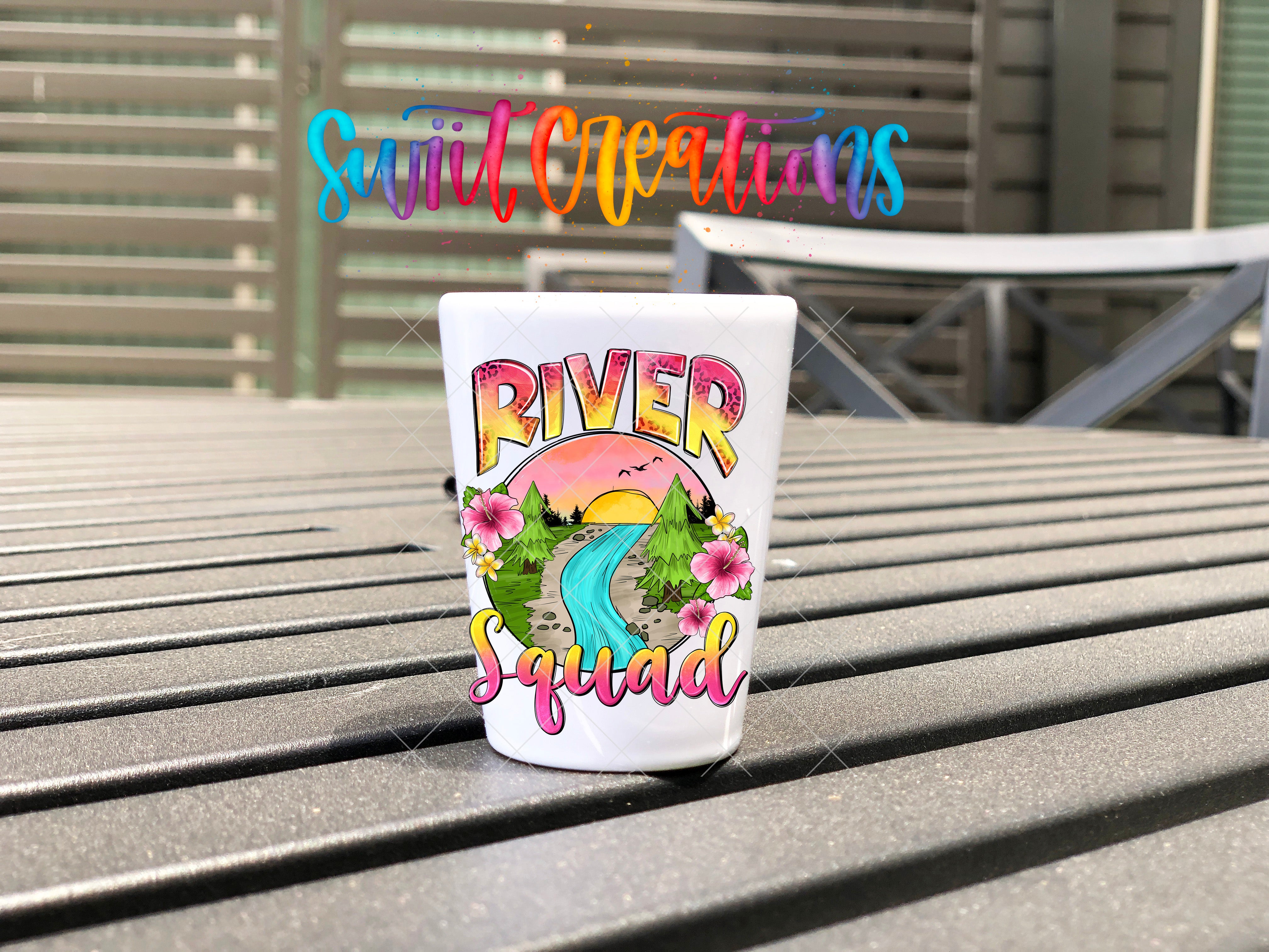 A colorful shot glass with the text "RIVER SQUAD" printed on it, placed on a wooden surface.