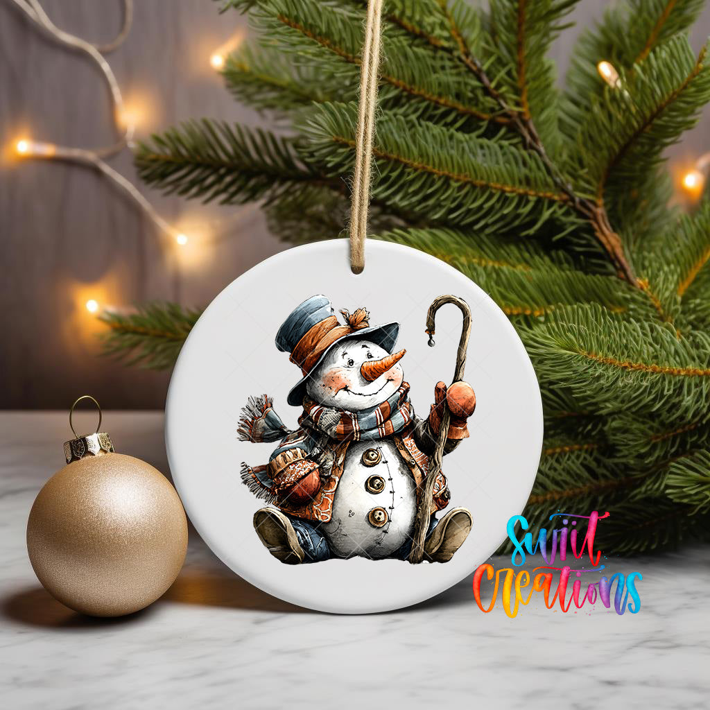 A white ornament featuring a snowman is displayed on a table, with a Christmas tree and a gold ornament visible in the background.