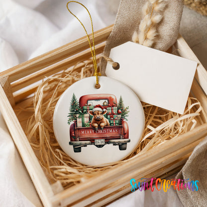 A white ceramic ornament with a red truck and Christmas decorations, including a Santa hat and presents, is displayed in a wooden crate.
