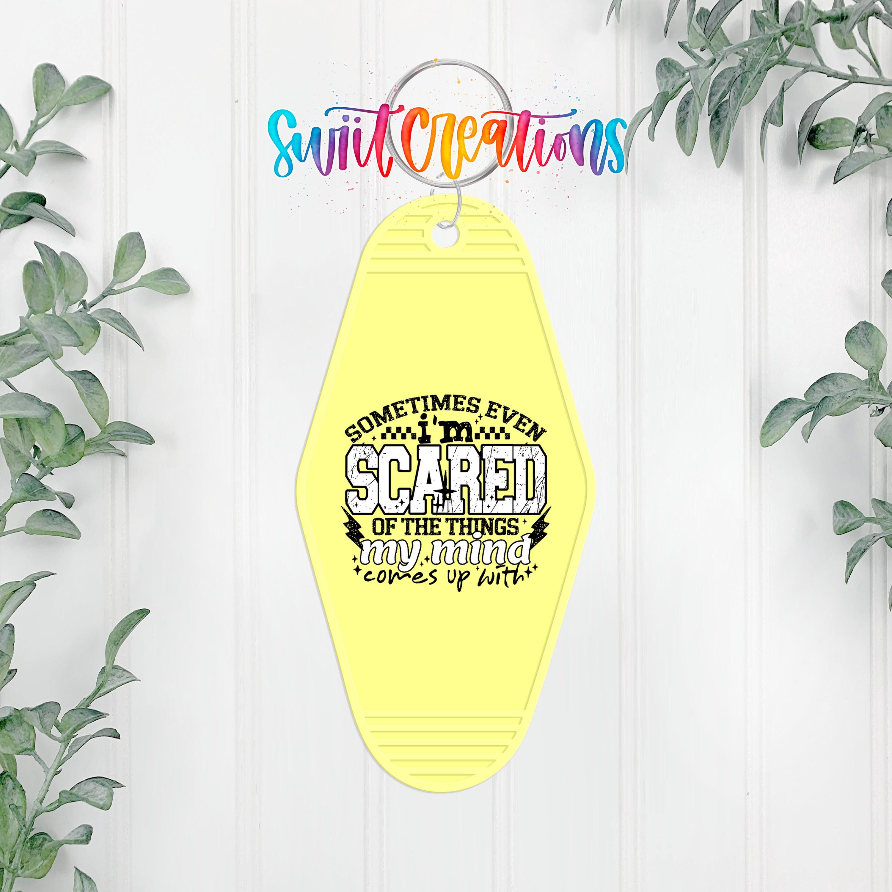 A yellow keychain with a printed message that says "Sometimes even scared of the things my mind comes up with" is hanging on a white wall.