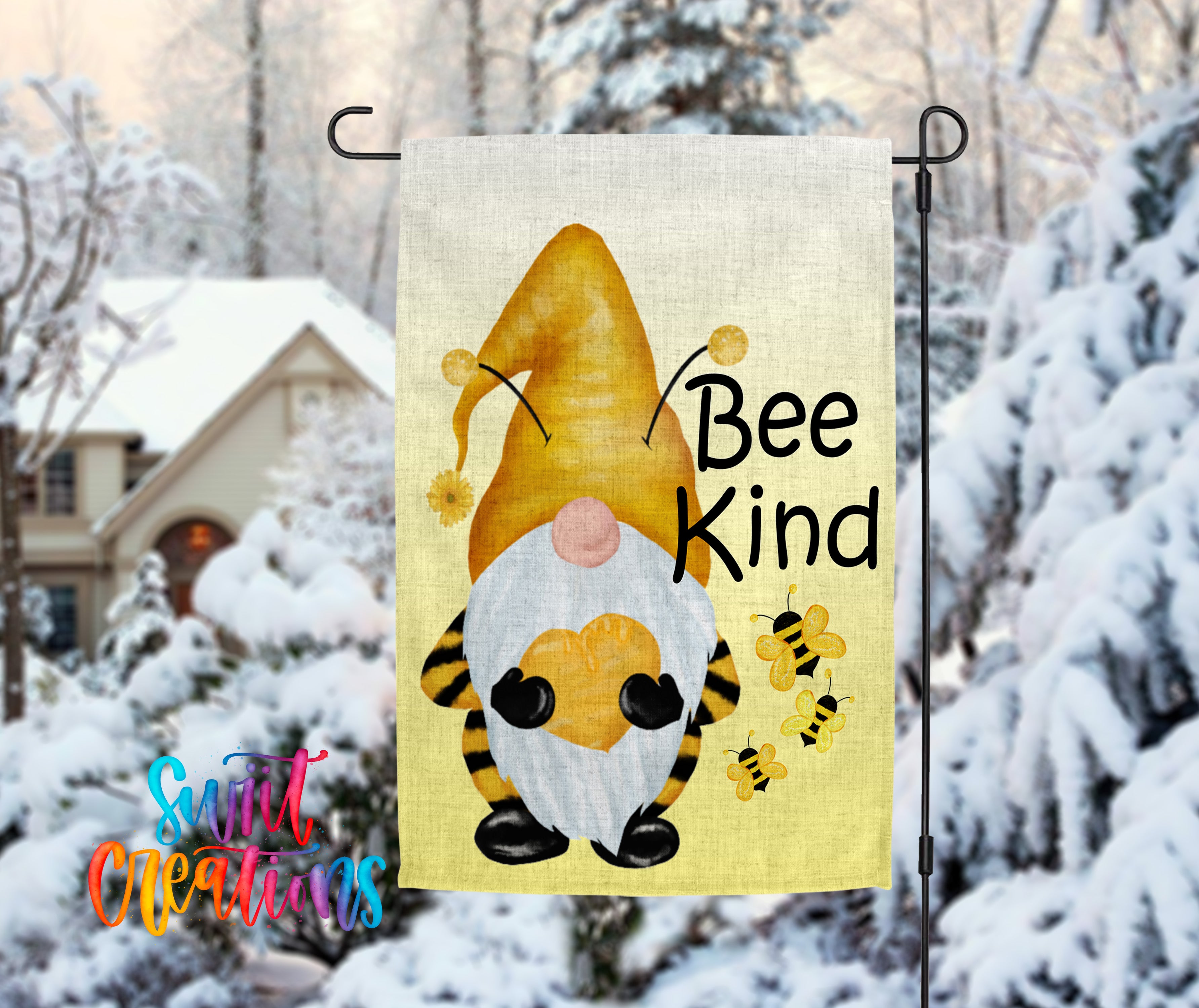 A garden gnome with a yellow hat and a bee on its back, along with the text "Bee Kind" is displayed on a flag, set against a snowy background with a house and trees in the distance.