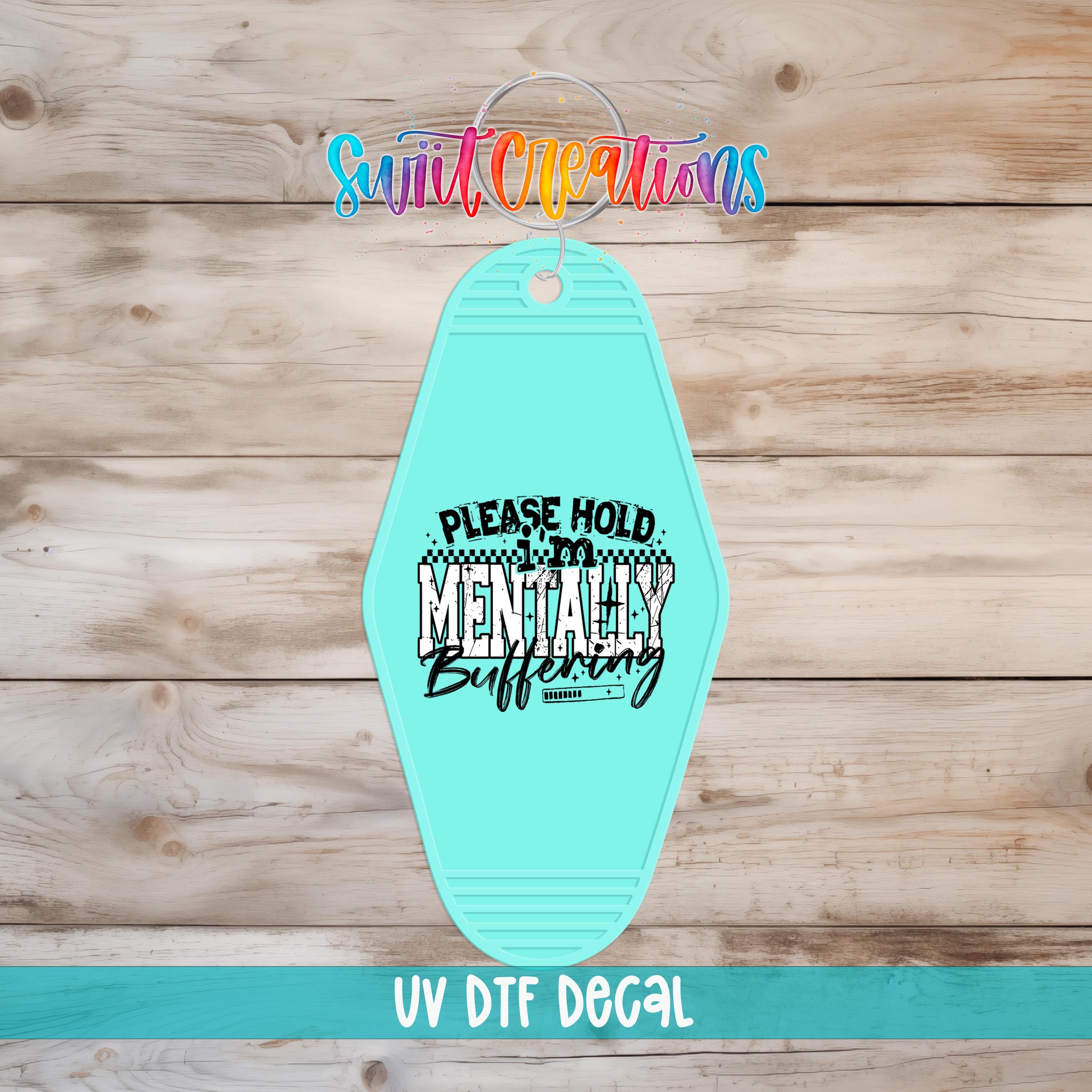 A turquoise keychain with a humorous text message printed on it, placed on a wooden surface.