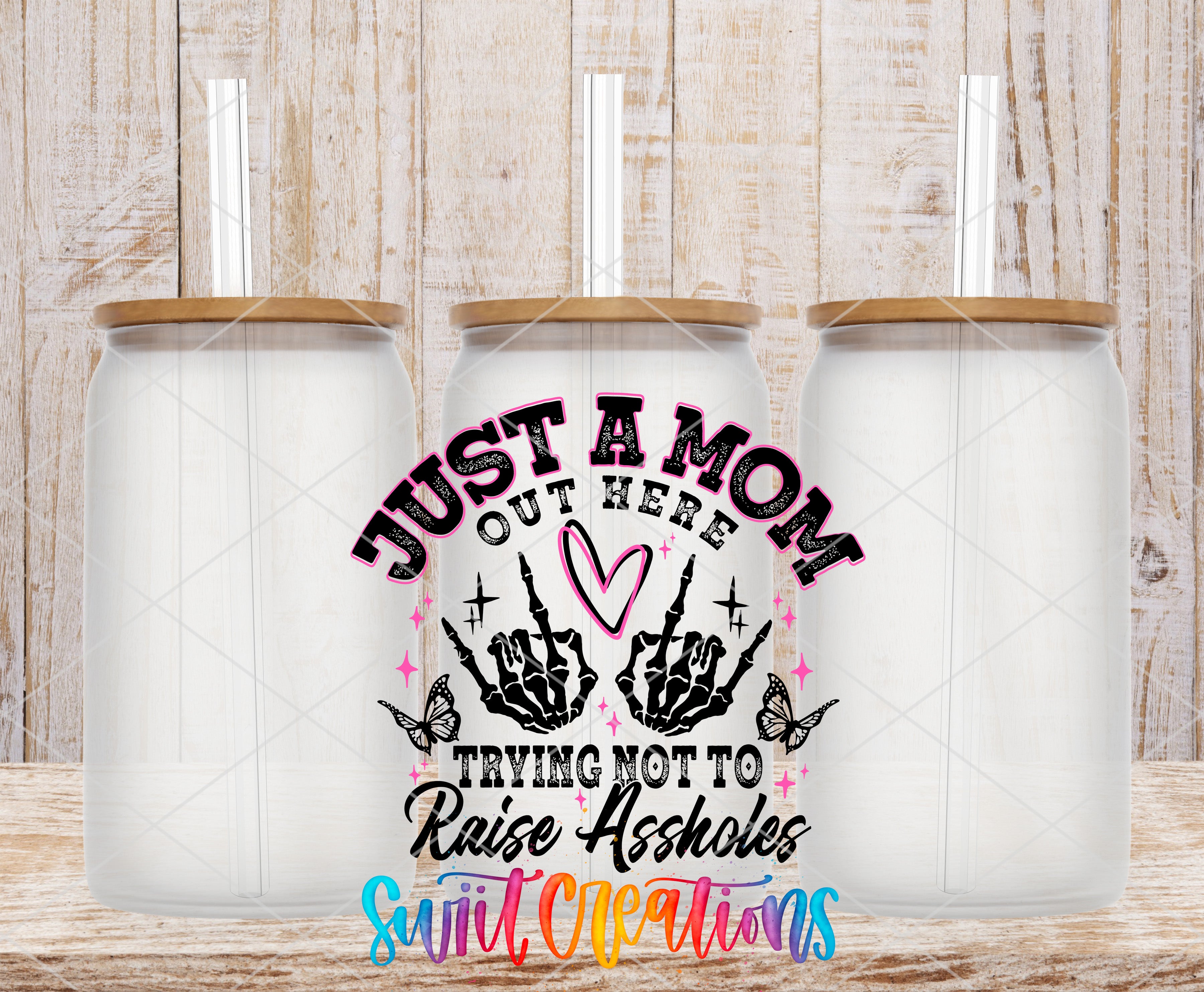 three clear glass jars with lids, arranged in a row against a wooden background. The jars have a unique design with a skull and crossbones motif. The text on the jars reads "Just a mom out here trying not to raise assholes" and "Swift cleanliness".