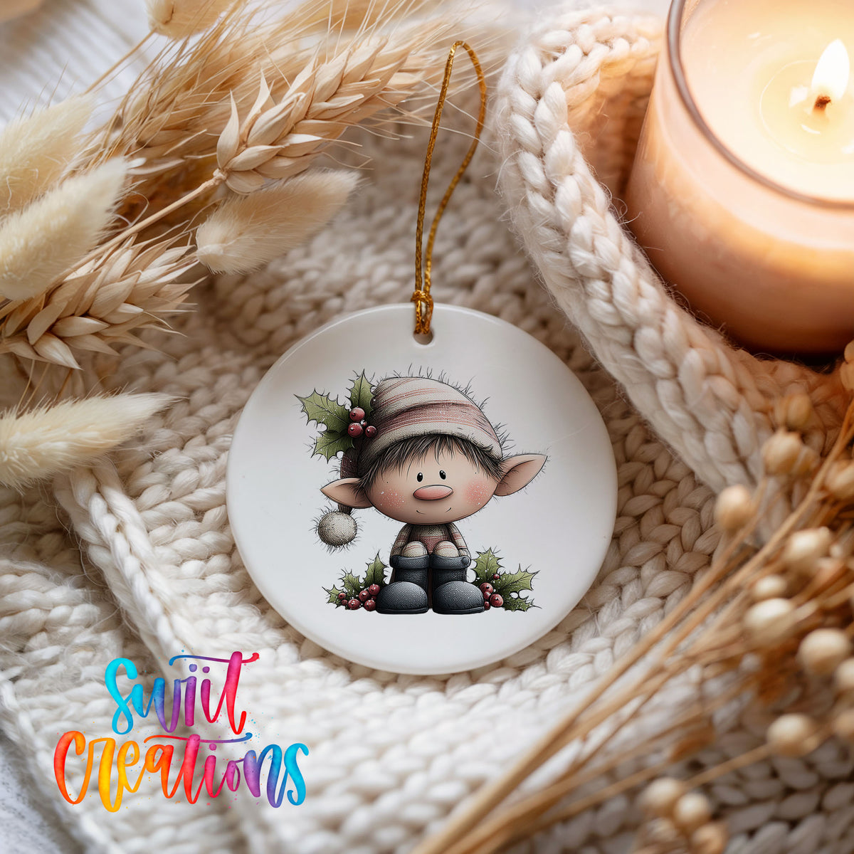 A white ornament featuring a cartoon elf sitting on a branch, surrounded by holly leaves and berries, is displayed on a white knitted surface.
