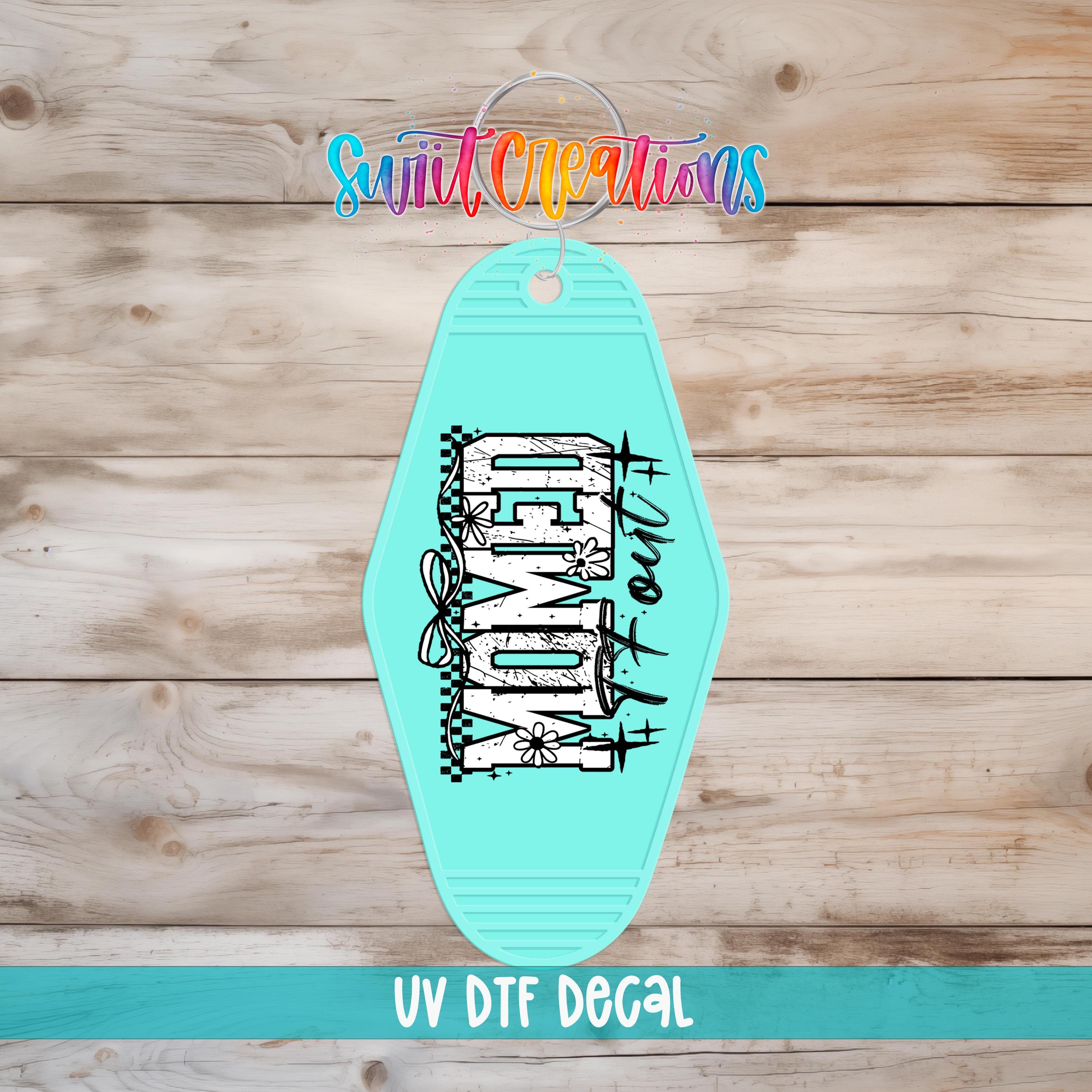 A turquoise-colored keychain with the word "DAMN" printed on it, placed on a wooden surface.