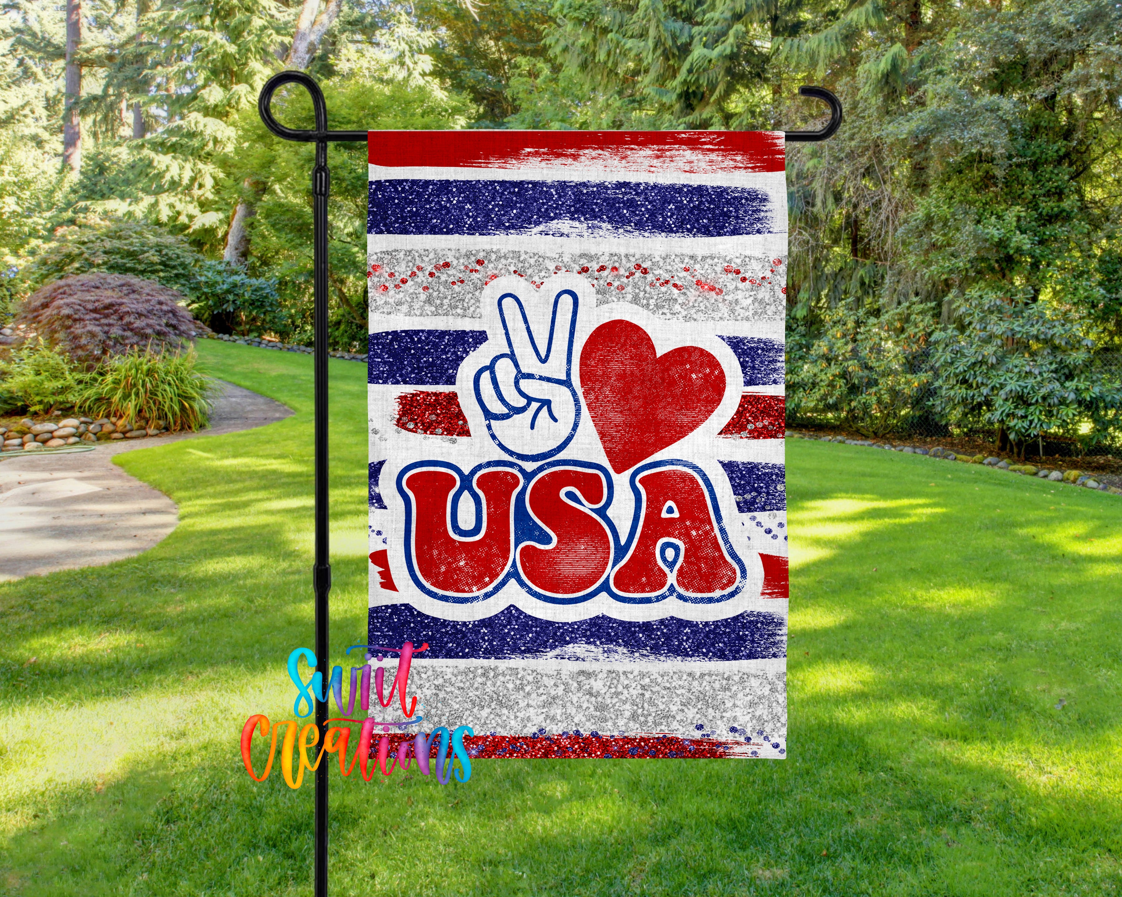A patriotic flag with the word "USA" prominently displayed, featuring a peace sign and a heart symbol. The flag is hanging in a grassy area surrounded by trees.