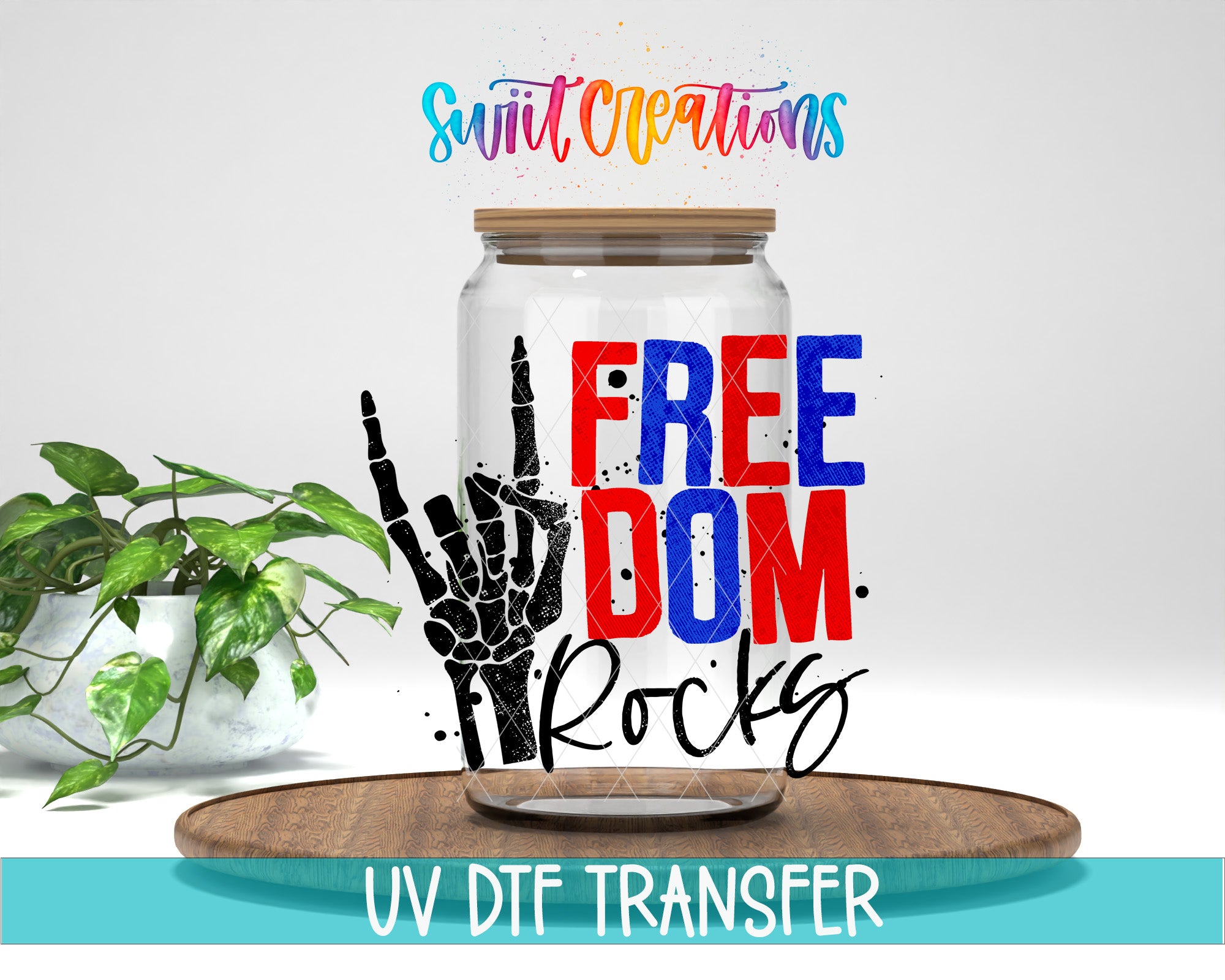 a glass jar with a hand-drawn skeleton hand making a peace sign, along with the text "FREE DOM ROCKS" and "Swift Creations" written above it. The jar is placed on a wooden surface, and there is a potted plant in the background.