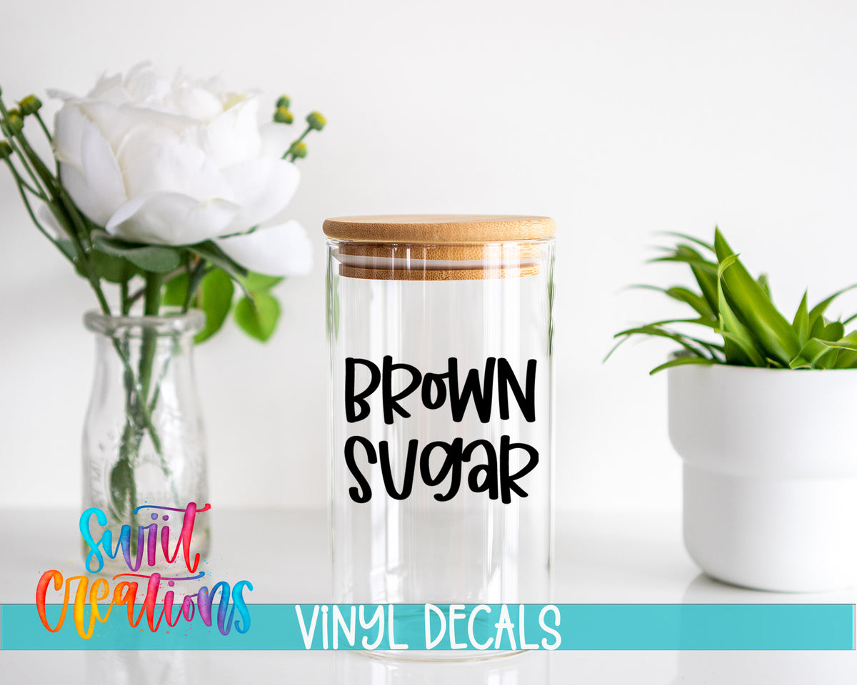 a clear glass jar with a wooden lid, placed on a white surface next to a vase with white flowers and a potted plant.