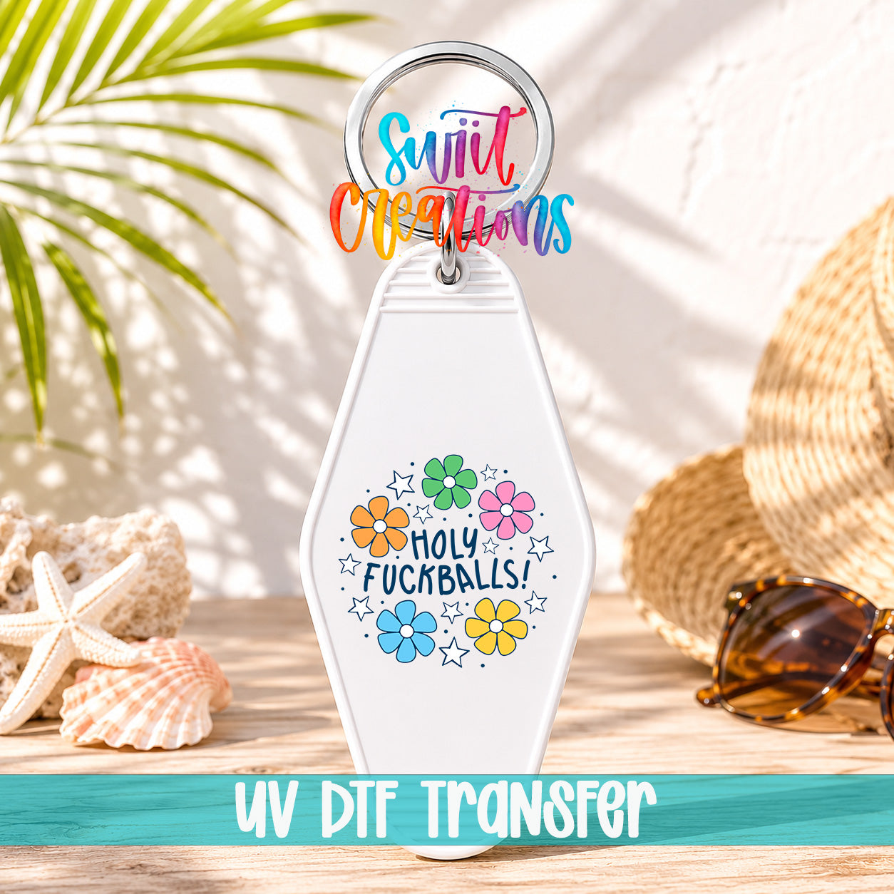 A keychain with a colorful design and text, placed on a wooden surface with sunglasses and a straw hat in the background.