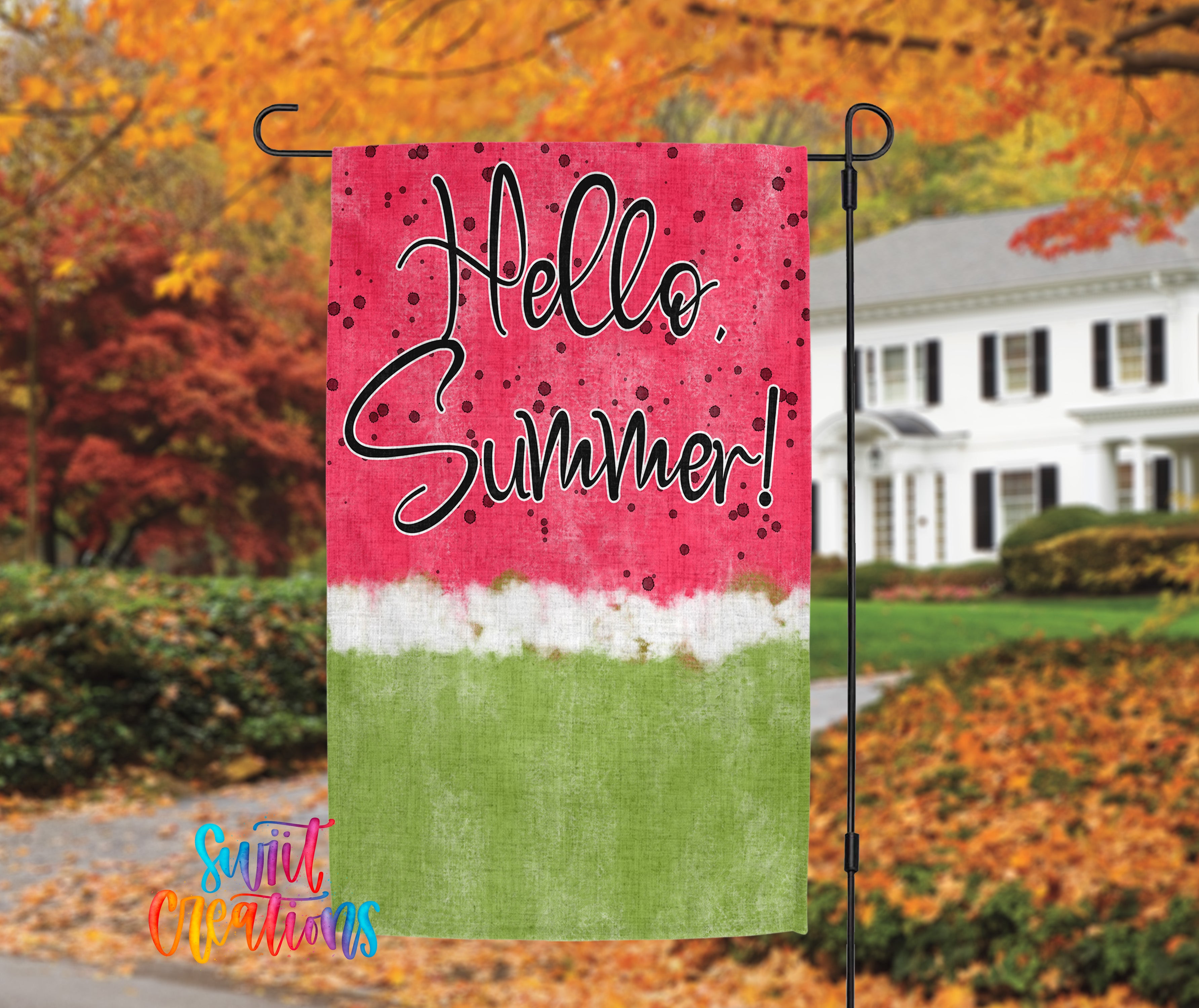 A colorful flag with the text "Hello Summer!" displayed prominently, hanging on a metal pole in front of a house with autumn foliage in the background.