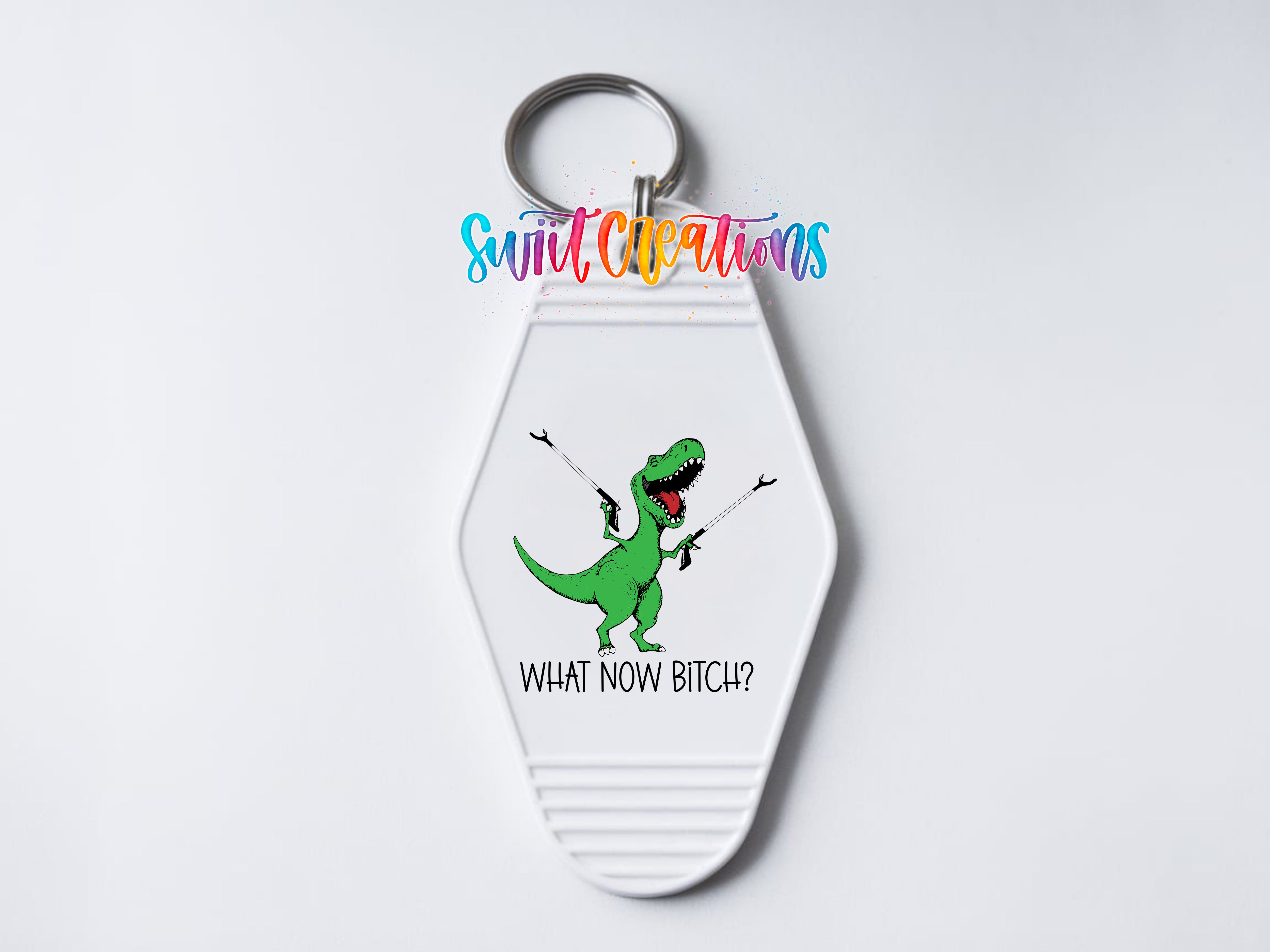 A keychain with a cartoon dinosaur and the text "WHAT NOW BITCH?" printed on it.