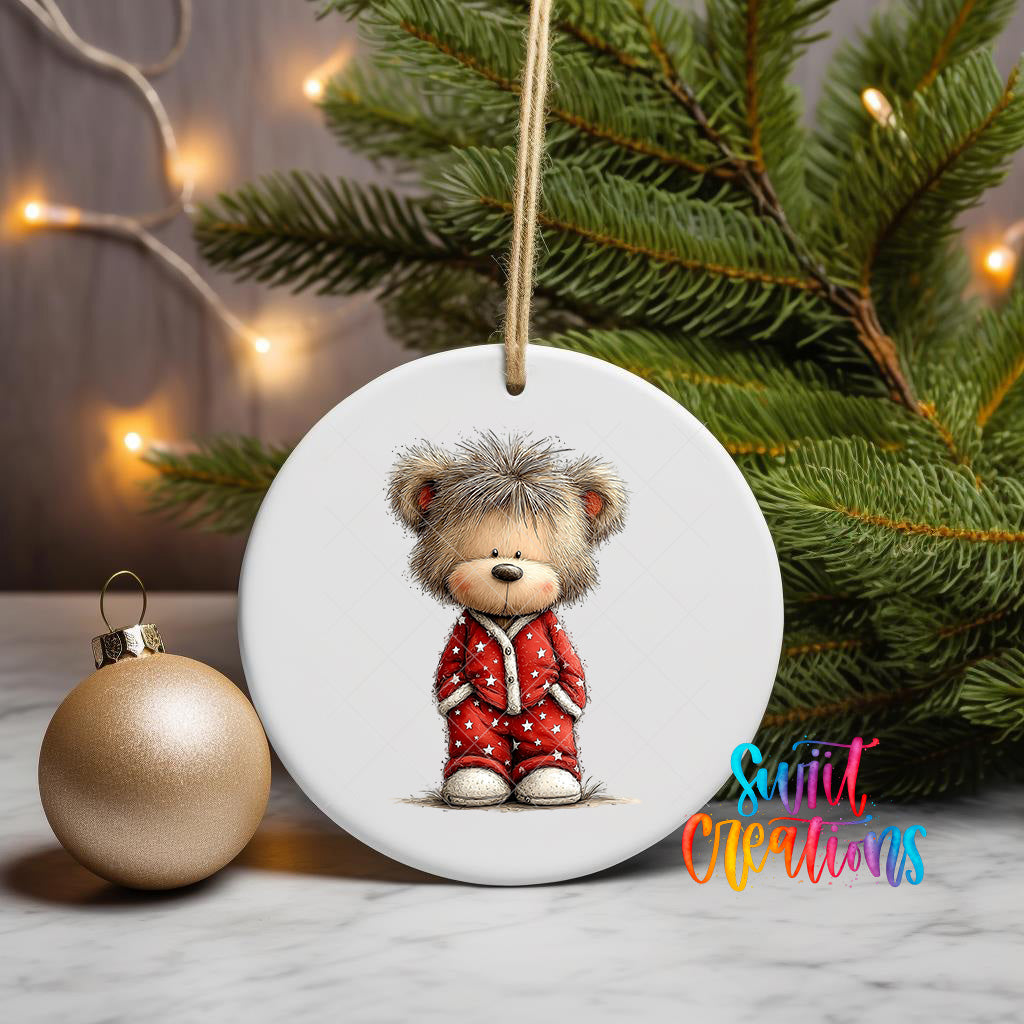 A white ceramic ornament featuring a teddy bear wearing a red outfit, with a Christmas tree and twinkling lights in the background.