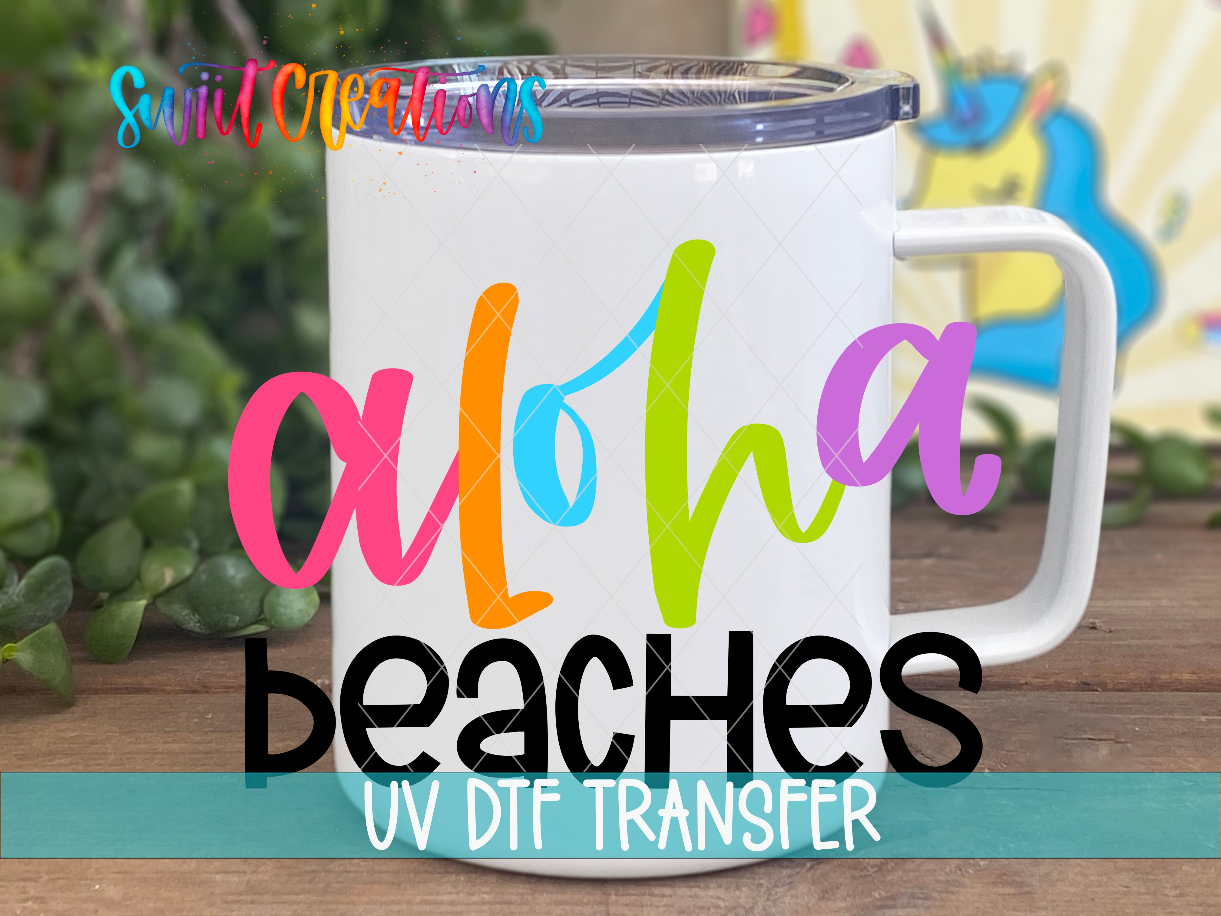 A white mug with colorful text that says "Aloha Beaches" and "UV DFT Transfer" printed on it.