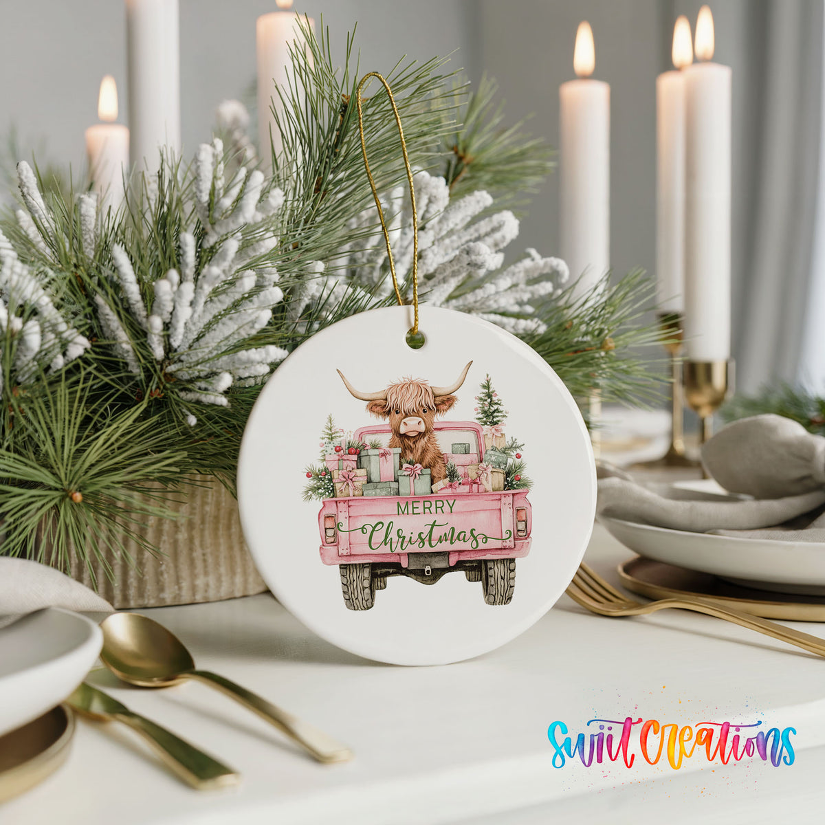 A white ceramic ornament with a pink truck and a cow decoration, surrounded by pine branches and candles, placed on a table.