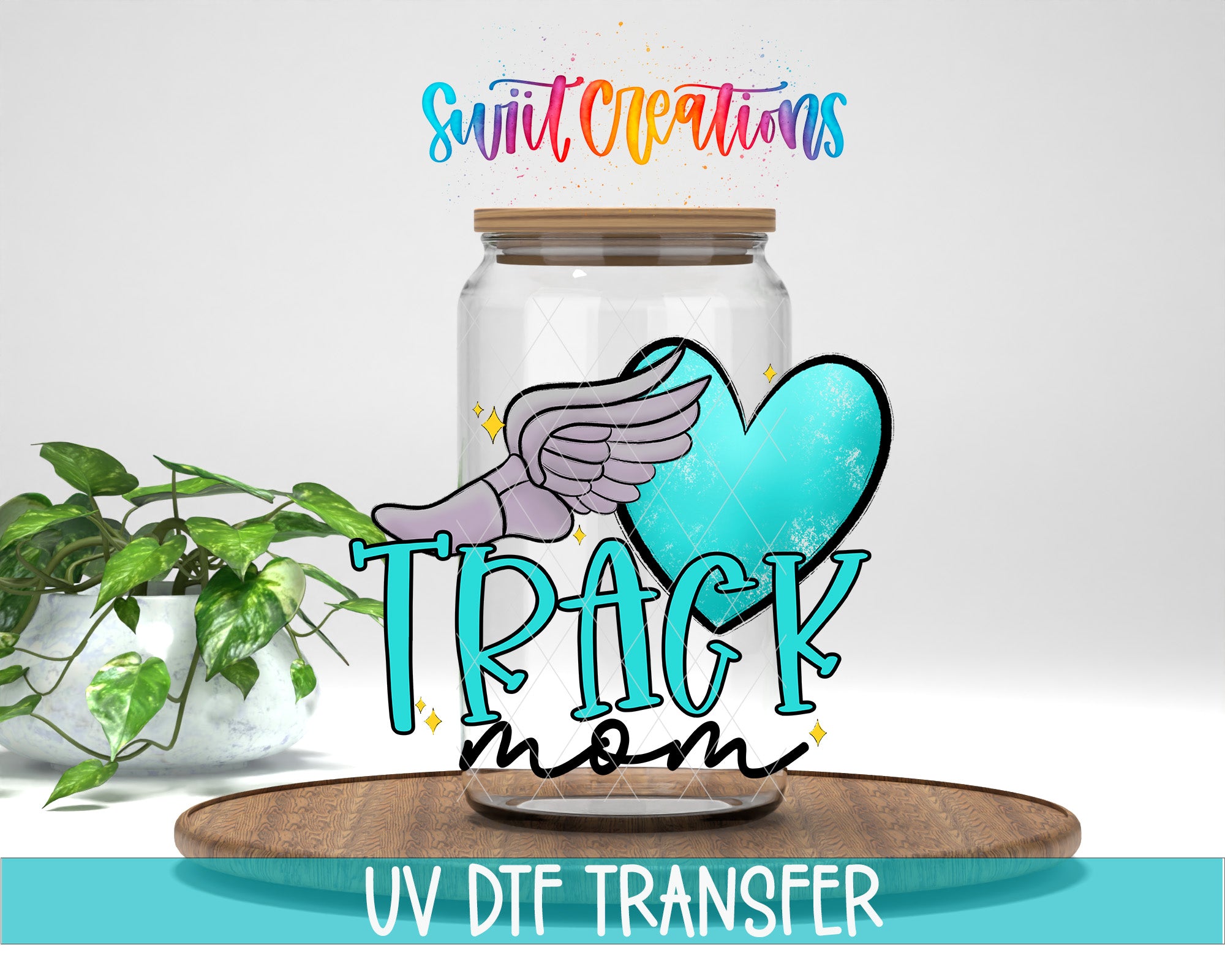 a glass jar with a winged design and the text "TRACK mom" on it, placed on a wooden surface.