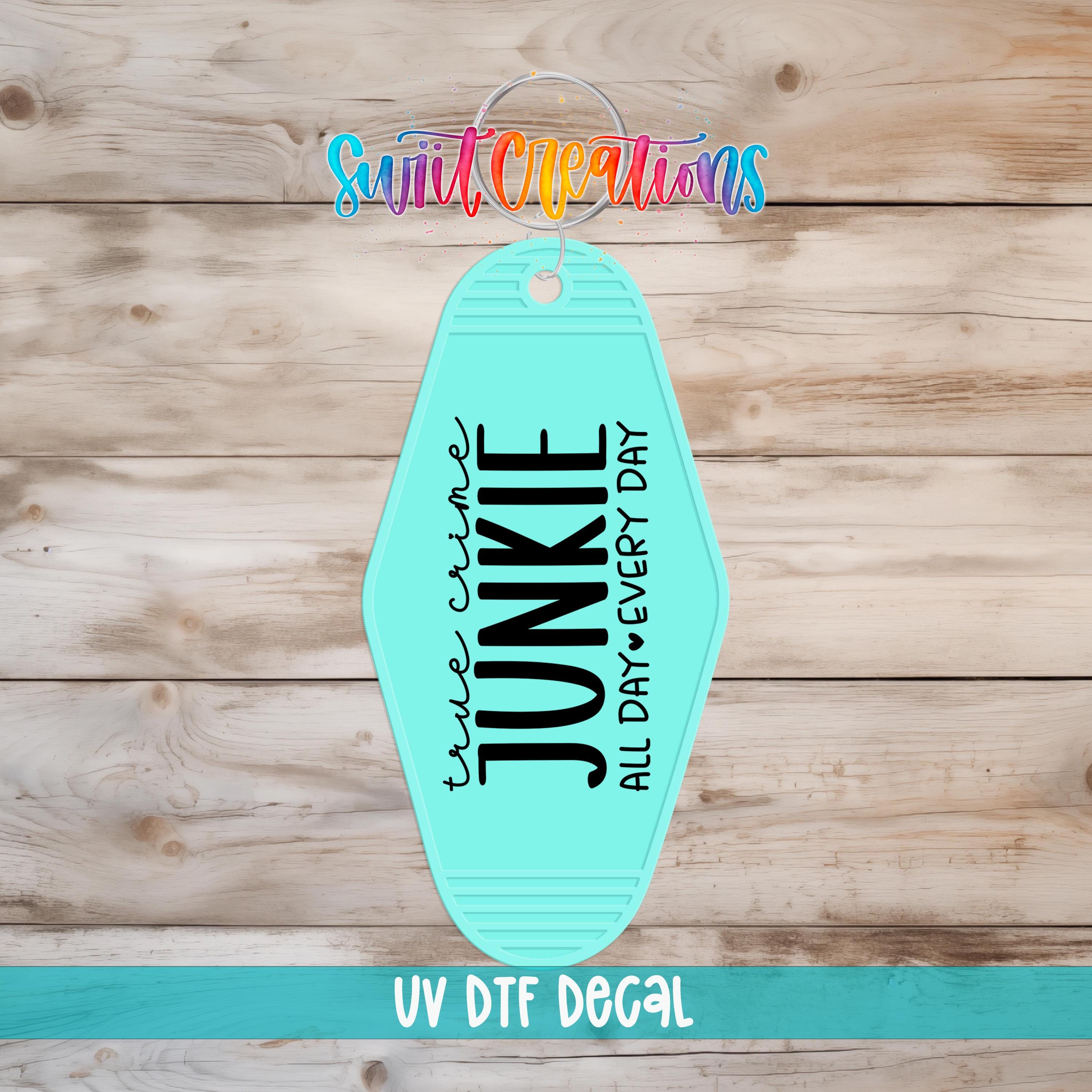 A turquoise-colored keychain with the text "True Crime Junkie All Day Every Day" printed on it, along with a colorful logo and the text "UV Dtf Decal" at the bottom.