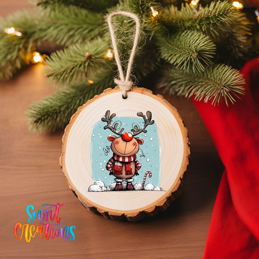 A wooden ornament featuring a cartoon reindeer with antlers, wearing a red scarf and standing in the snow, hanging on a Christmas tree.