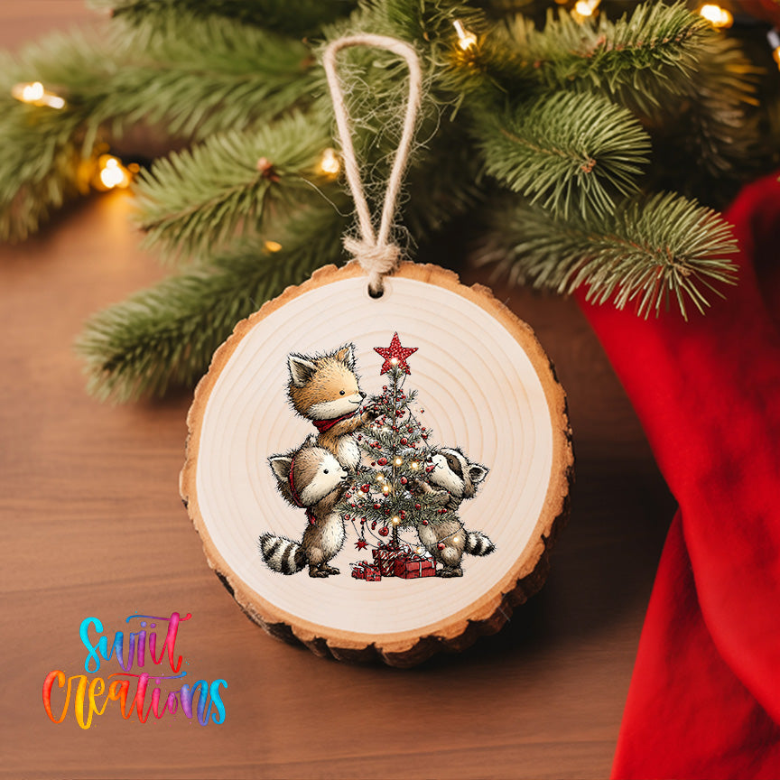 A wooden ornament featuring a fox and two raccoons decorating a Christmas tree, with a star on top.