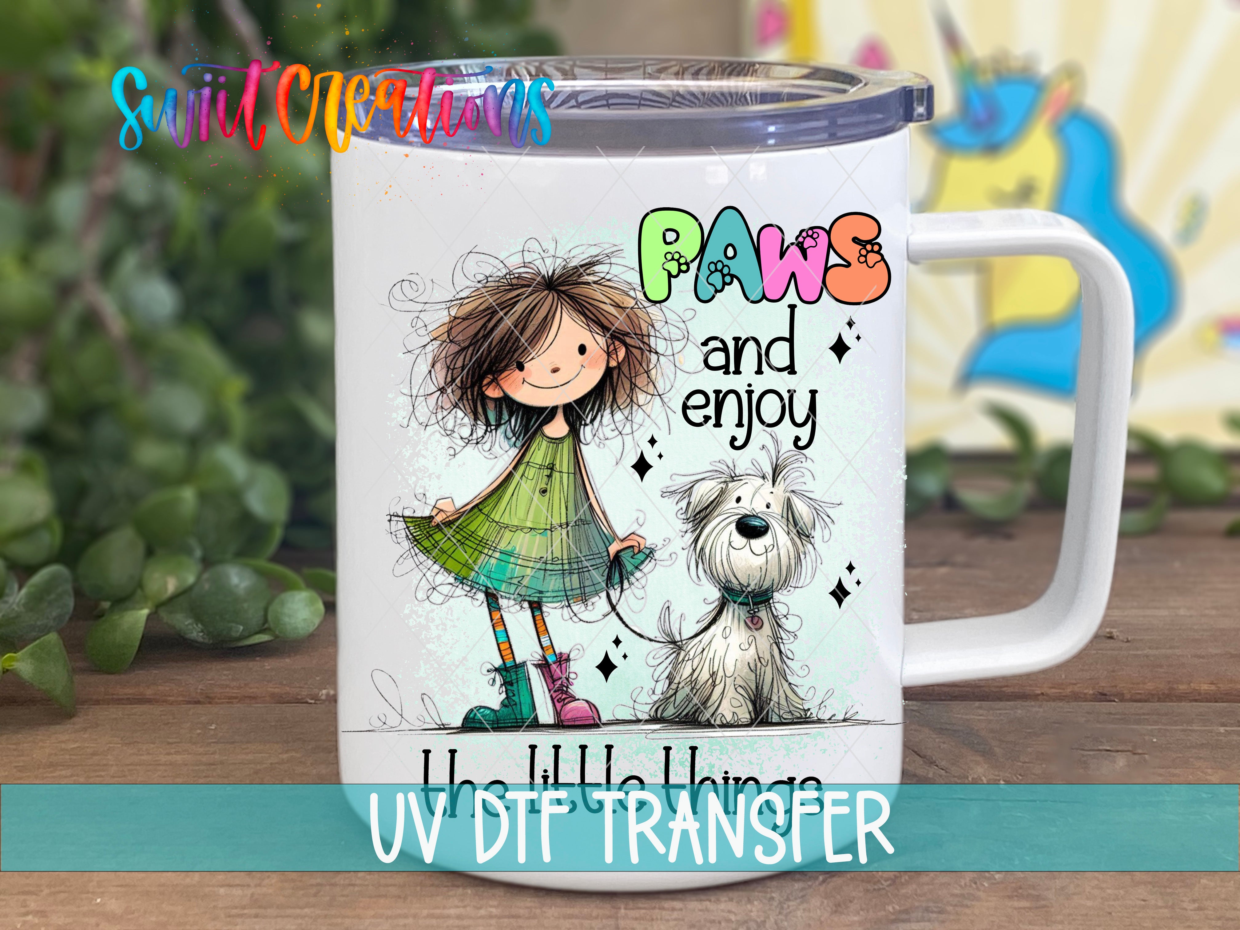 A white mug with a colorful illustration of a girl and a dog, along with the text "Paws and enjoy" and "UV DIT TRANSFER".