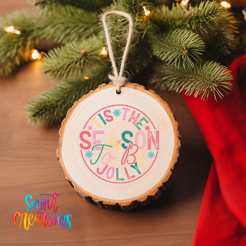 A wooden ornament with a colorful design hangs on a Christmas tree, surrounded by pine branches and twinkling lights.