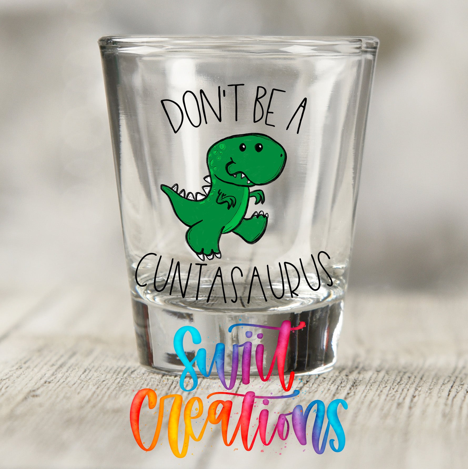 a shot glass with a cartoon dinosaur and text on it.
