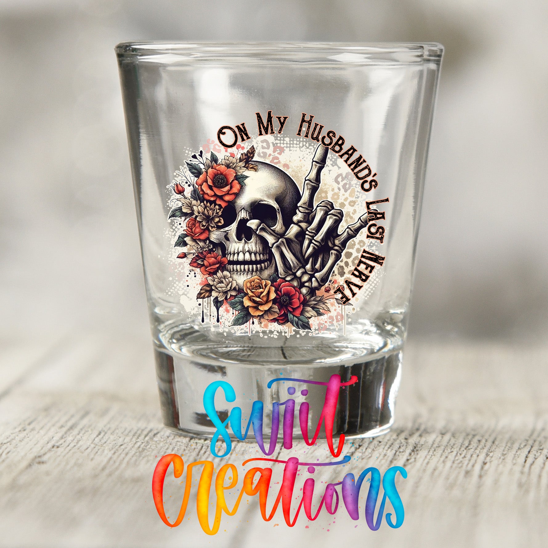 A shot glass with a skull design and floral elements, along with the text "On My Husband's Last Meal" printed on it.