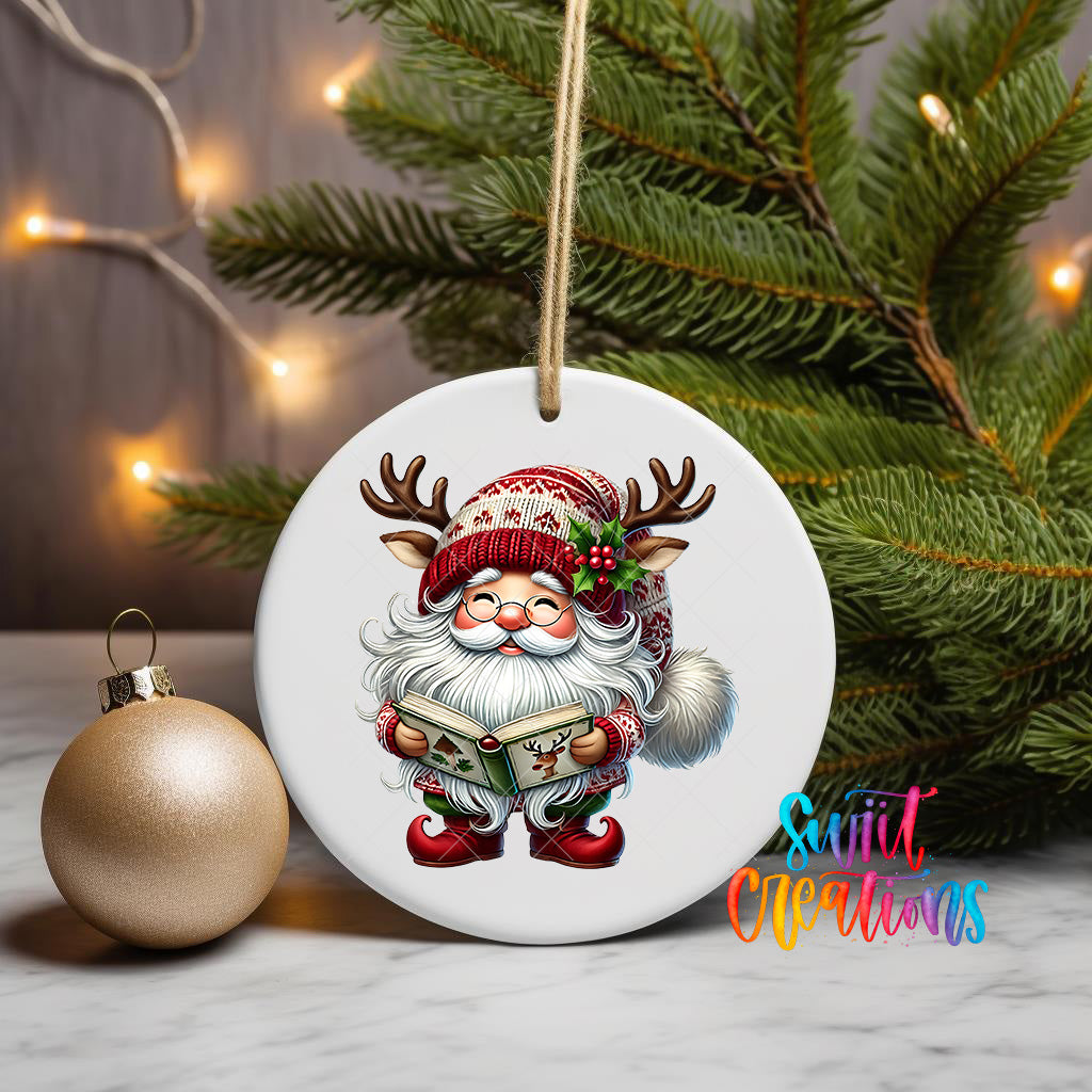 A white ornament featuring a cartoon Santa Claus holding a book and wearing antlers, with a Christmas tree and twinkling lights in the background.