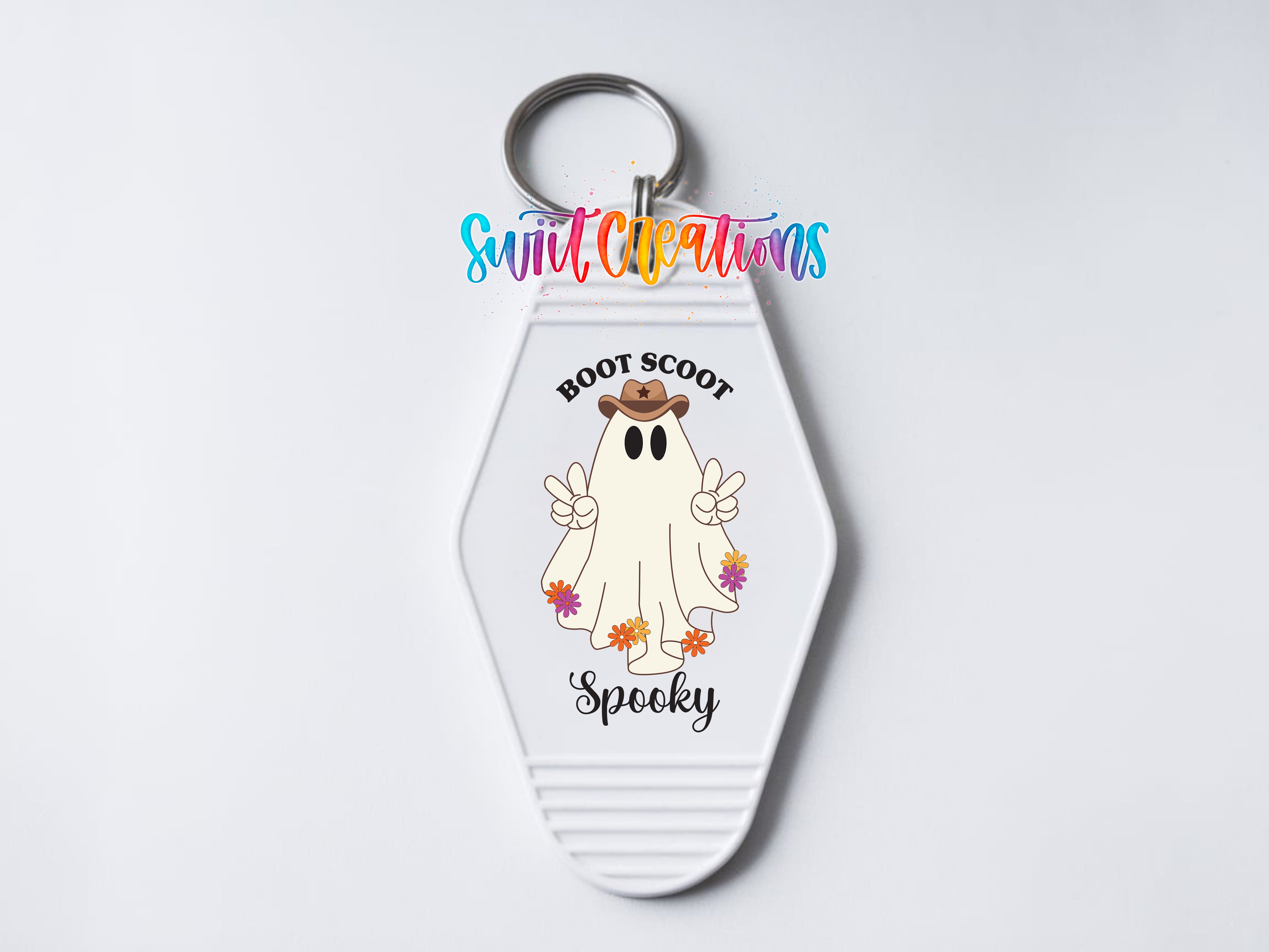 A keychain with a cartoon ghost wearing a cowboy hat and holding a peace sign, with the text "Boot Scoot Spooky" printed on it.