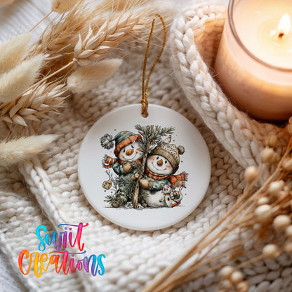 A ceramic ornament featuring two snowmen, one wearing a green hat and the other a red hat, is displayed on a knitted blanket. A lit candle is also present in the scene.