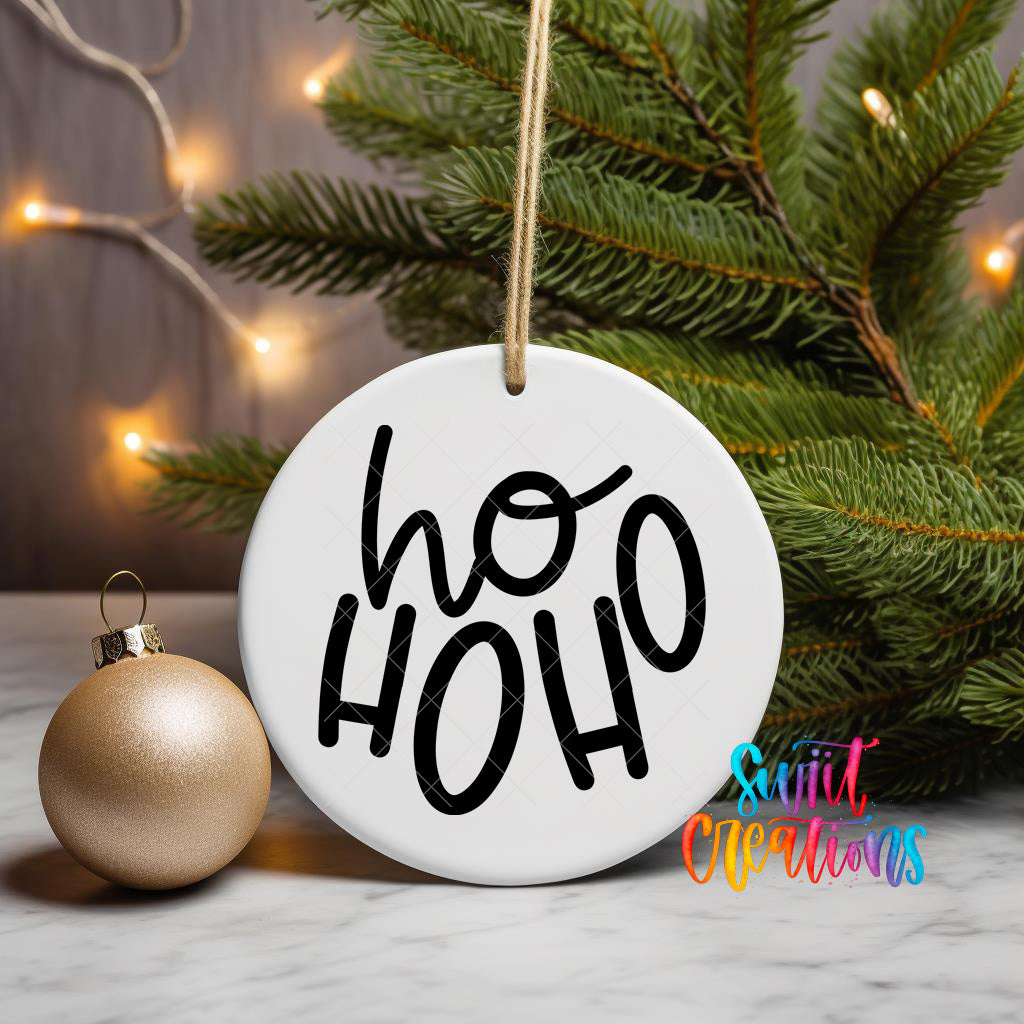 A white ornament with the text "ho ho ho" in black letters is hanging from a string, accompanied by a gold ornament and a pine tree with twinkling lights in the background.