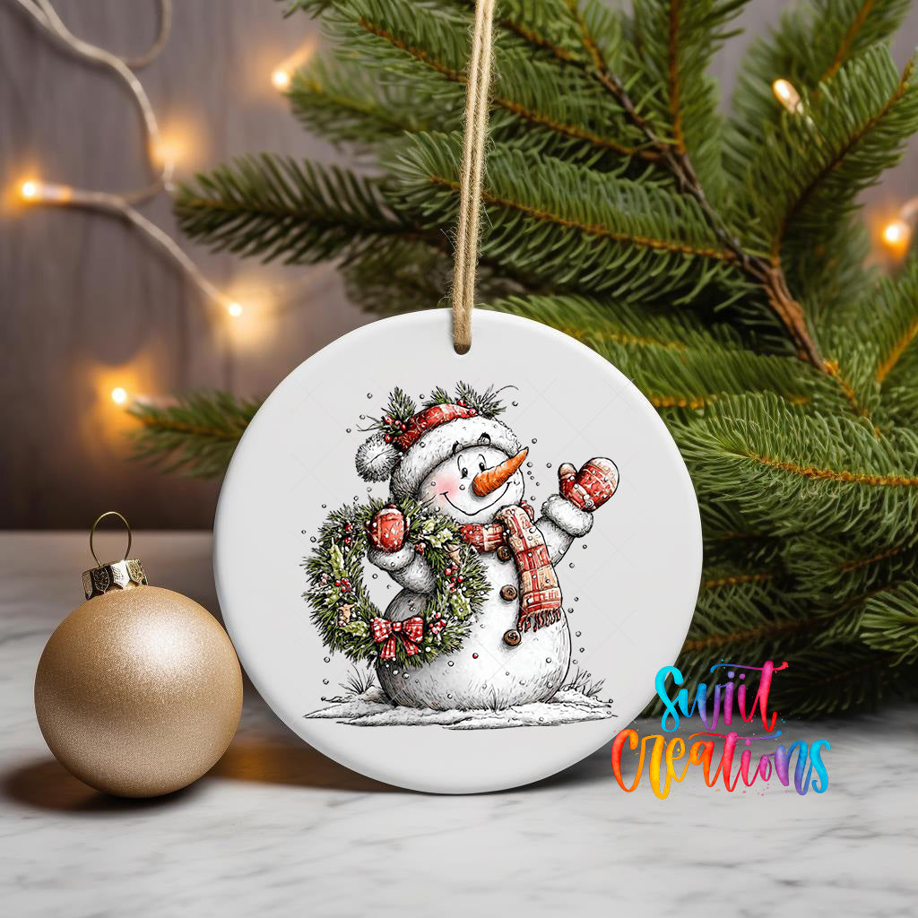 A white ceramic ornament featuring a snowman with a wreath and a carrot nose, surrounded by Christmas lights and a pine tree.