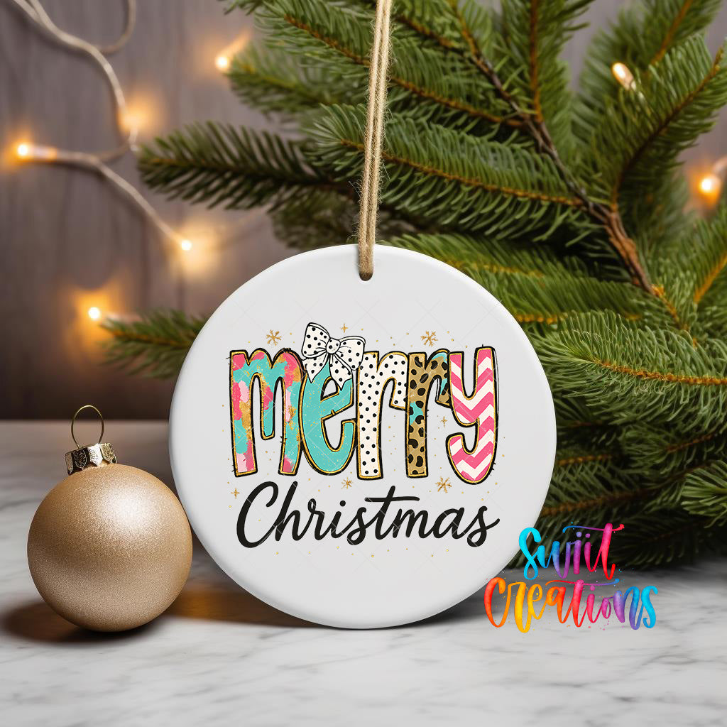 A white Christmas ornament with the text "MERRY CHRISTMAS" is displayed on a table, surrounded by a gold ornament and a pine tree with twinkling lights in the background.