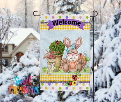 A colorful welcome sign featuring a cartoon rabbit sitting in a pot of flowers, with a snowy background and a house in the distance.