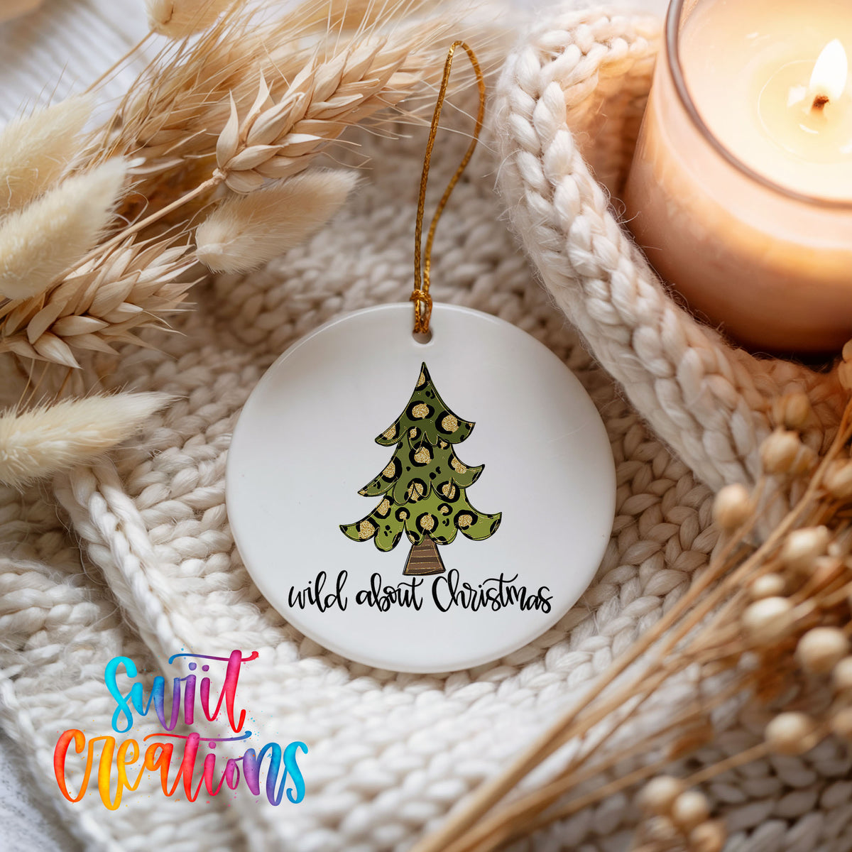 A white Christmas ornament with a leopard print tree design, hanging on a white knit blanket. The ornament has the text "wild about Christmas" written on it.